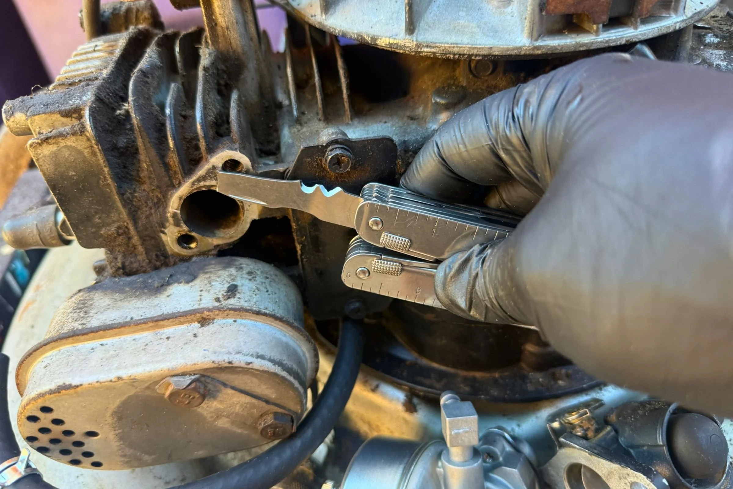 Using the Victorinox Swiss Tool X scraper to remove gasket residue from a lawnmower engine.