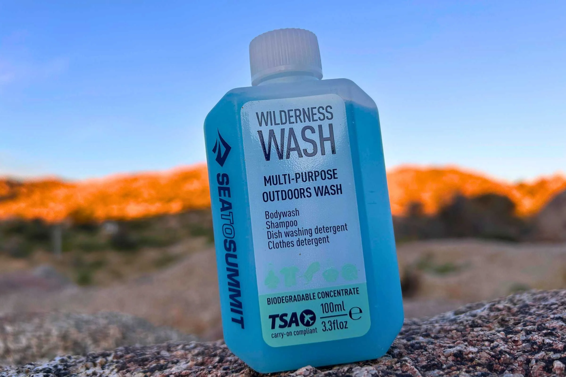 A bottle of Sea to Summit Wilderness Wash sits on a rock with a sunlit hill in the background