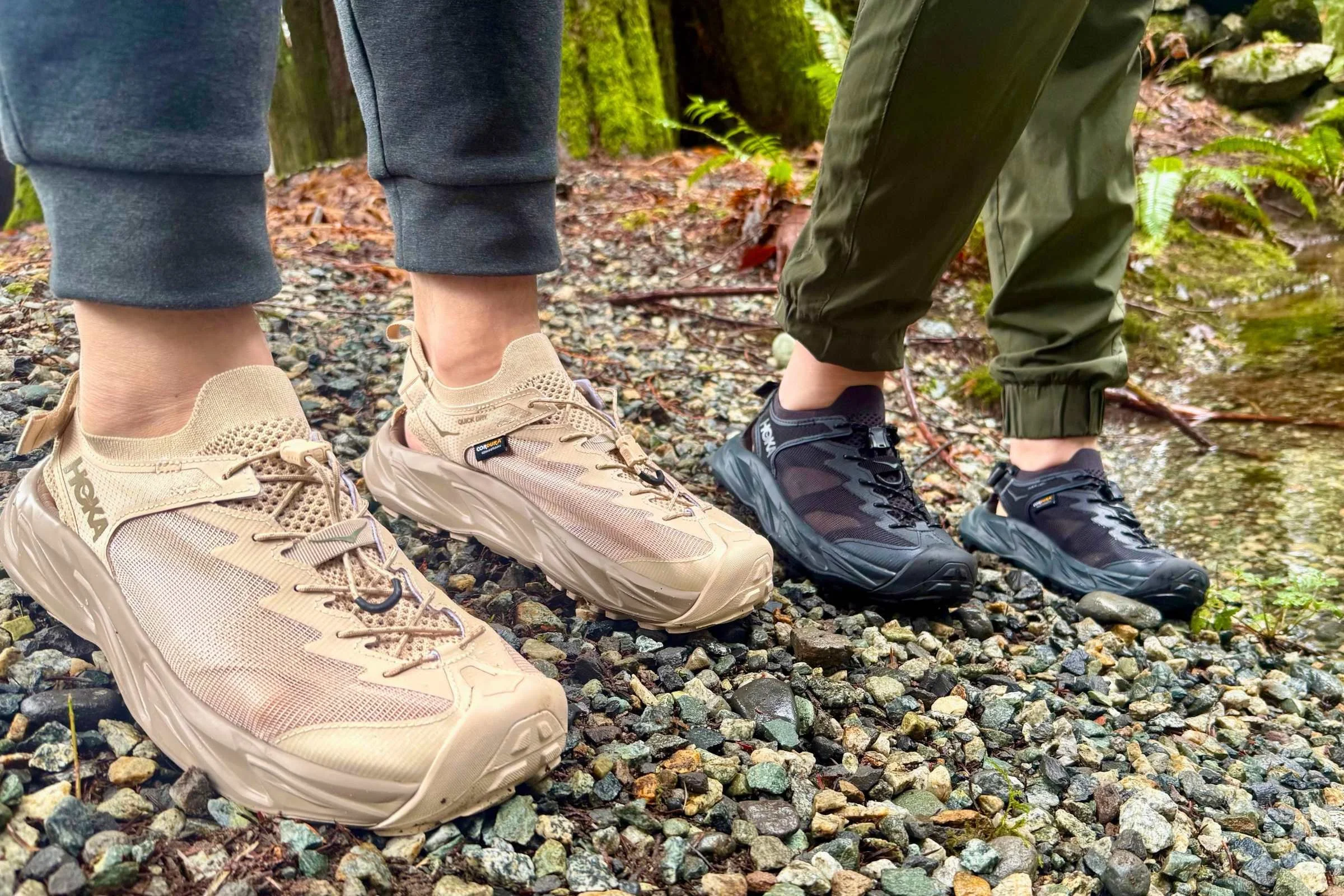 Two people standing on a gravel shore each wearing a pair of the HOKA Hopara 2 water shoes