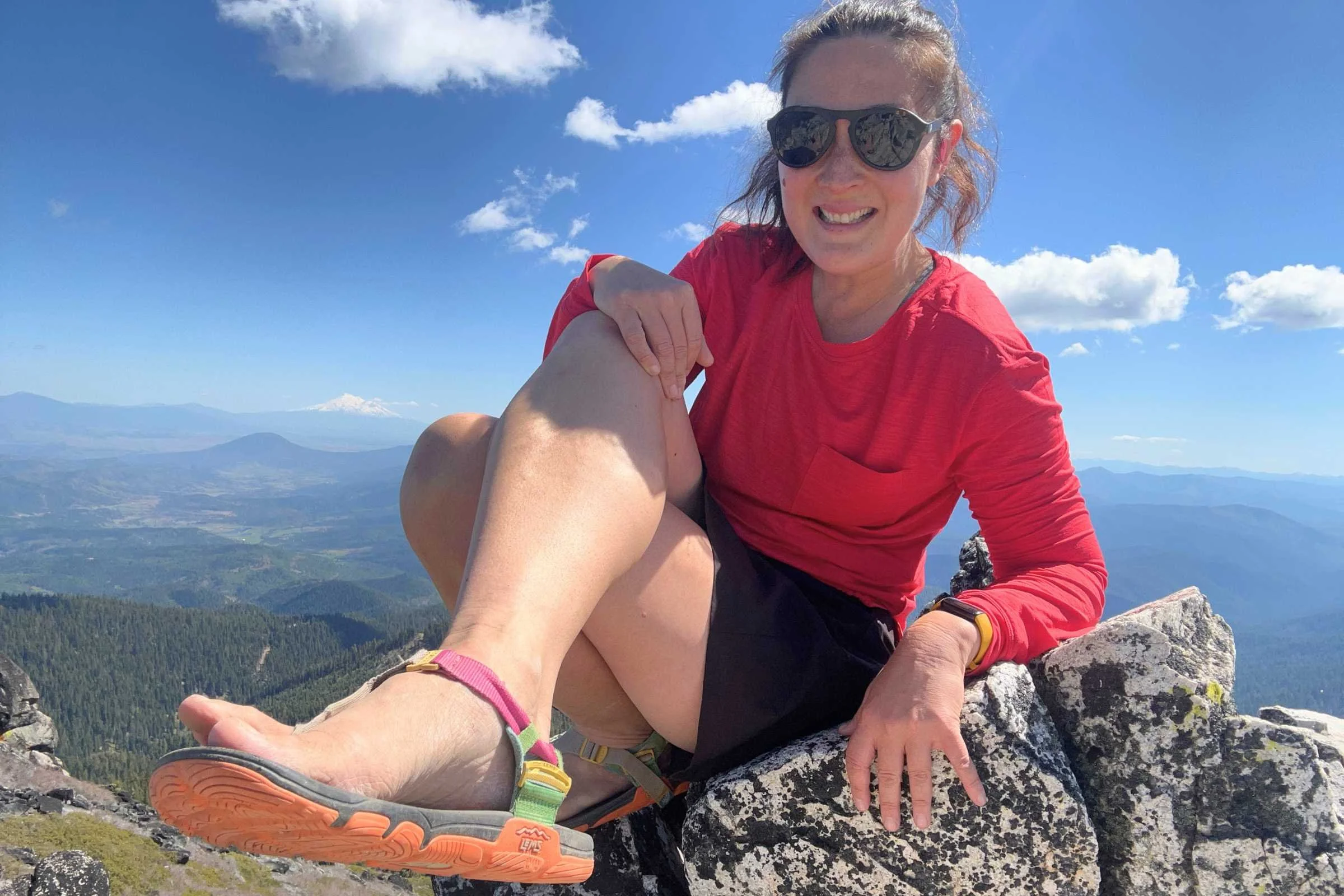 Liz Thomas modeling the Lems Switchback Sandal Knit while sitting on a rock with an expansive view in the backgroun