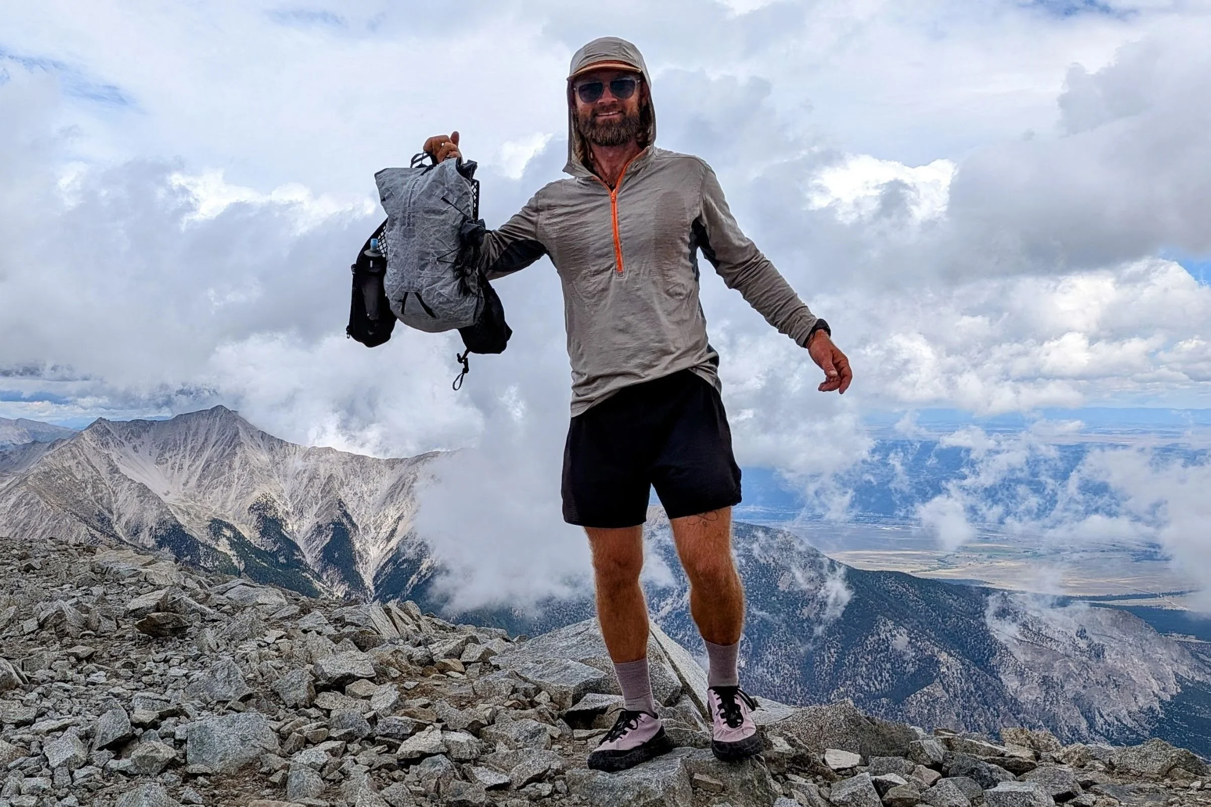 A man stands on a mountain peak holding the Black Diamond Distance 15 Backpack.