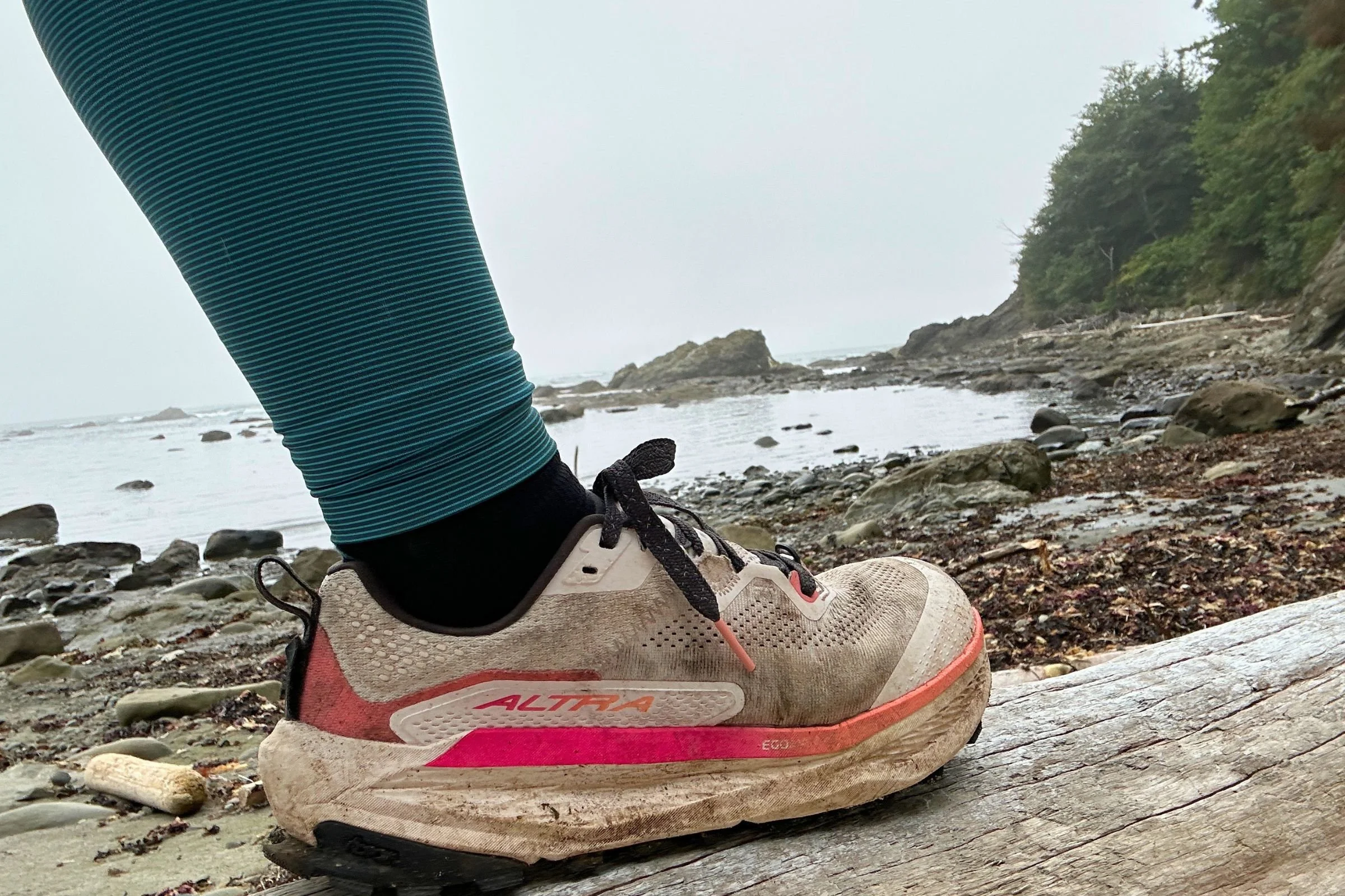 A person wearing the Altra Olympus 7 stands on a log in a wooded setting.