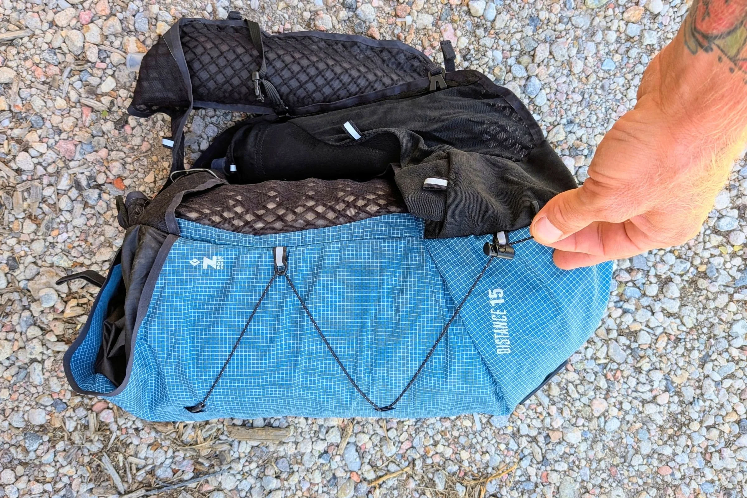 A person holds the Black Diamond Distance 15 Backpack beside another view of it on the ground.