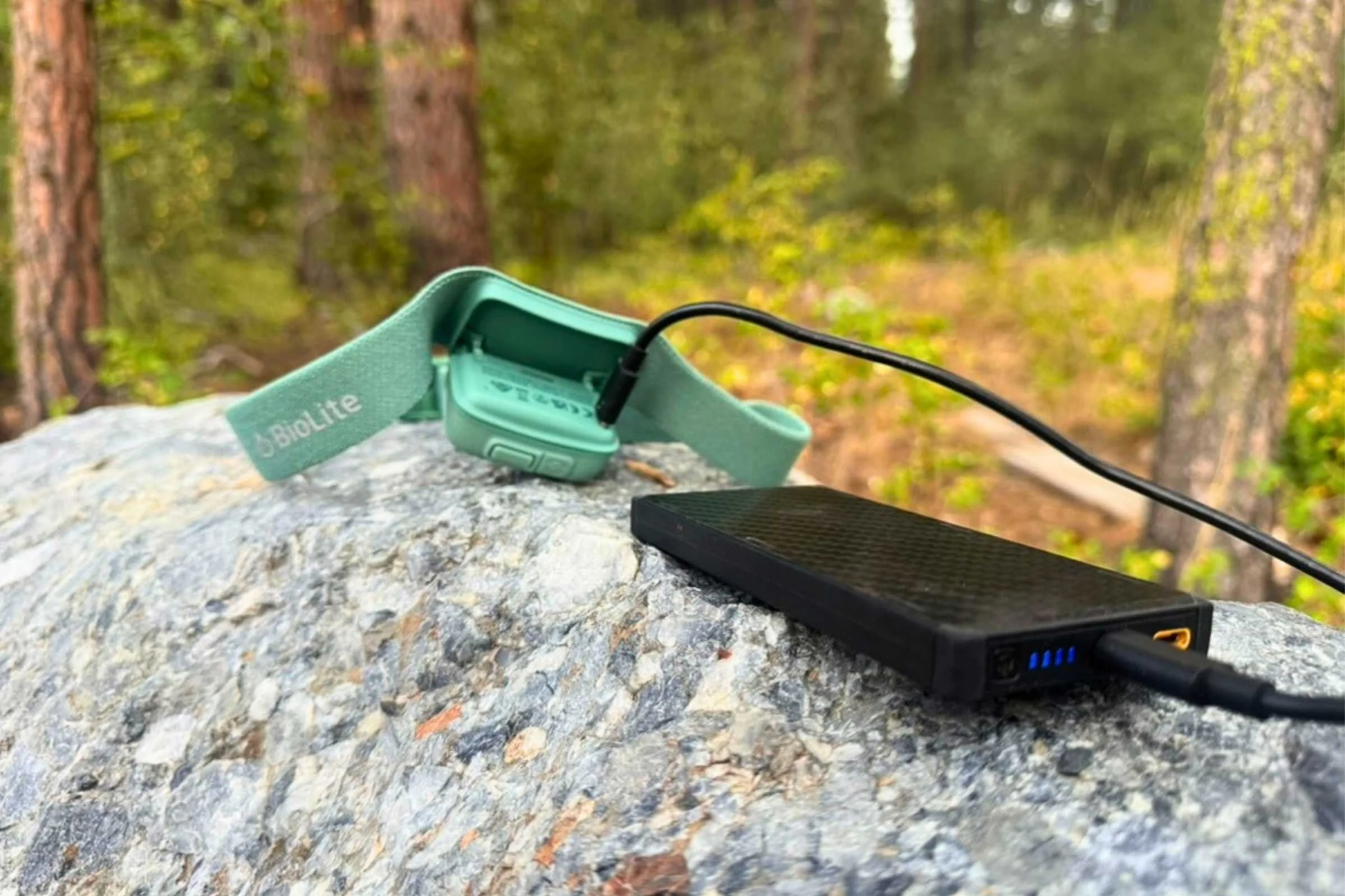 A green BioLite headlamp being charged by a power bank on top of a rock