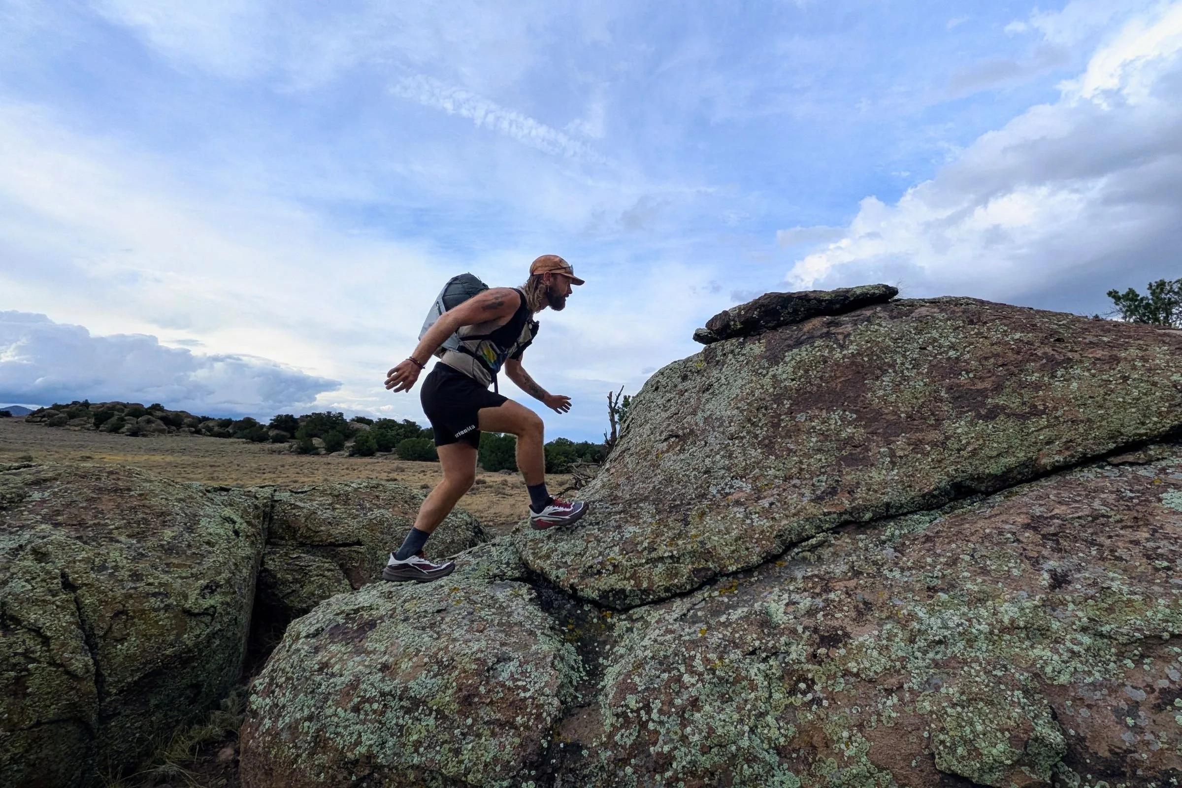 A man wearing Salomon Genesis 2 Trail Running Shoes climbs a large rock outdoors.