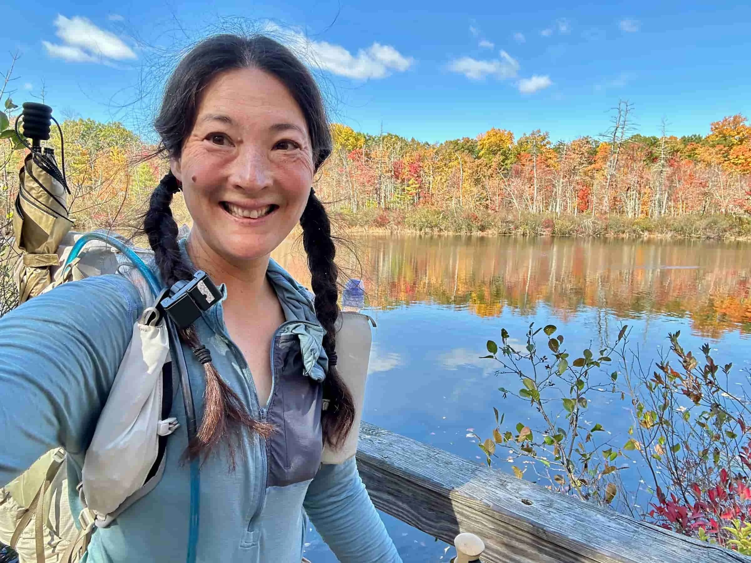 hiker liz thomas on the new england trail with fall color and a pond in the background