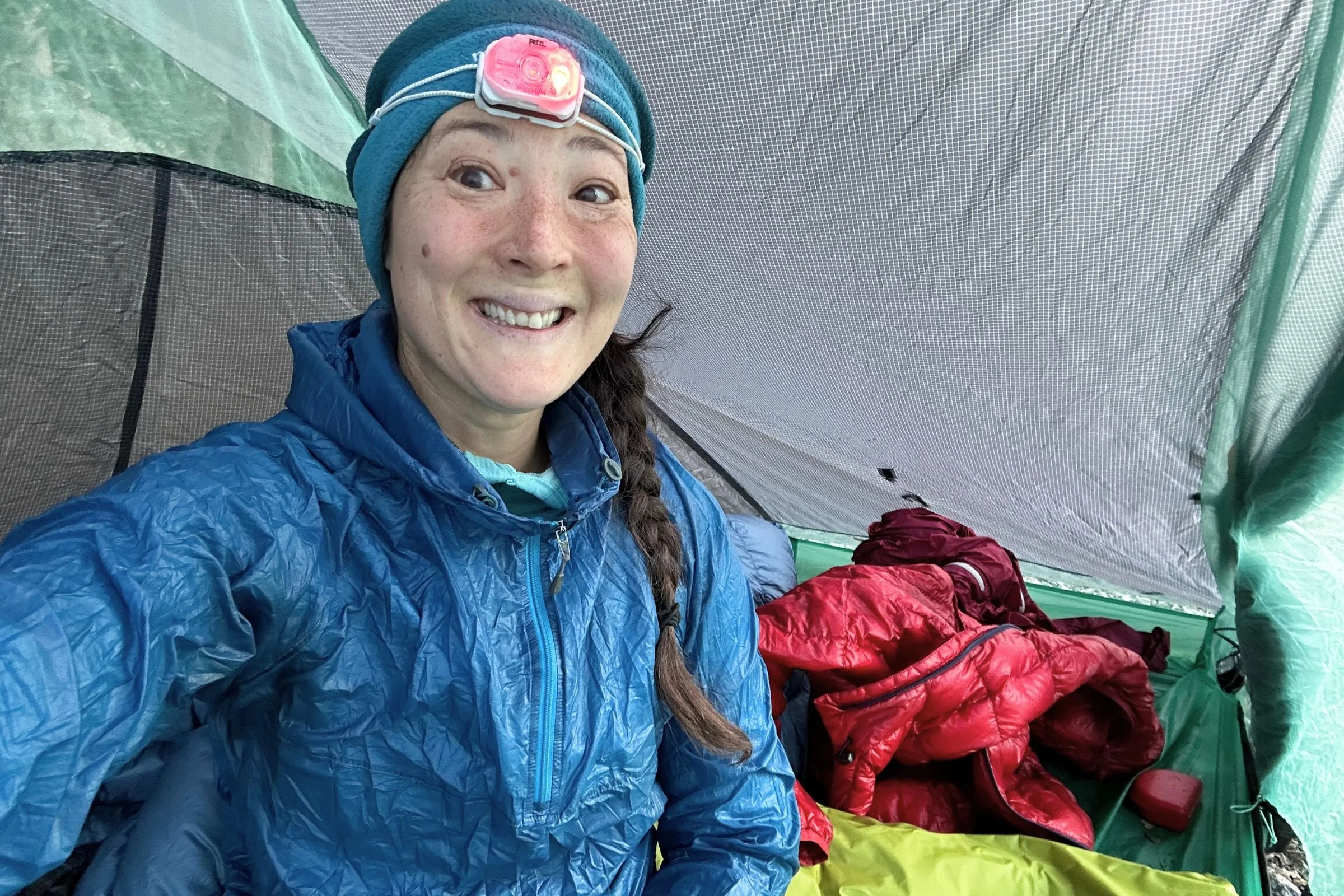 The author, inside a tent, wearing the Petzl Swift LT headlamp over a blue fleece hat.