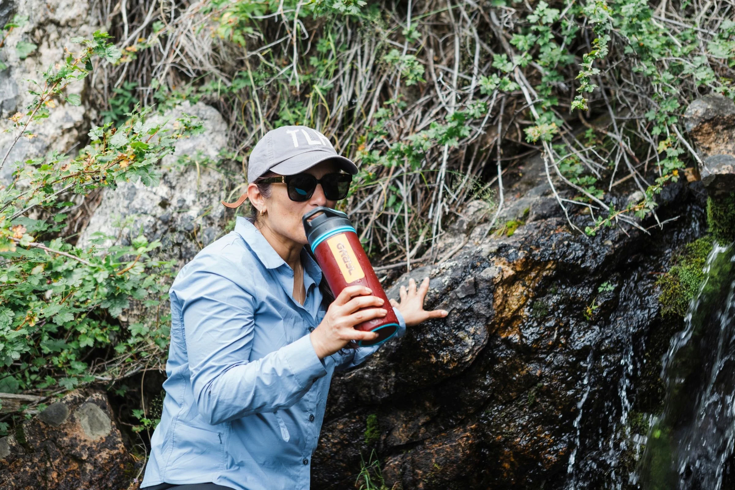 A woman holding a Grayl GeoPress Purifier in front of a waterfall.