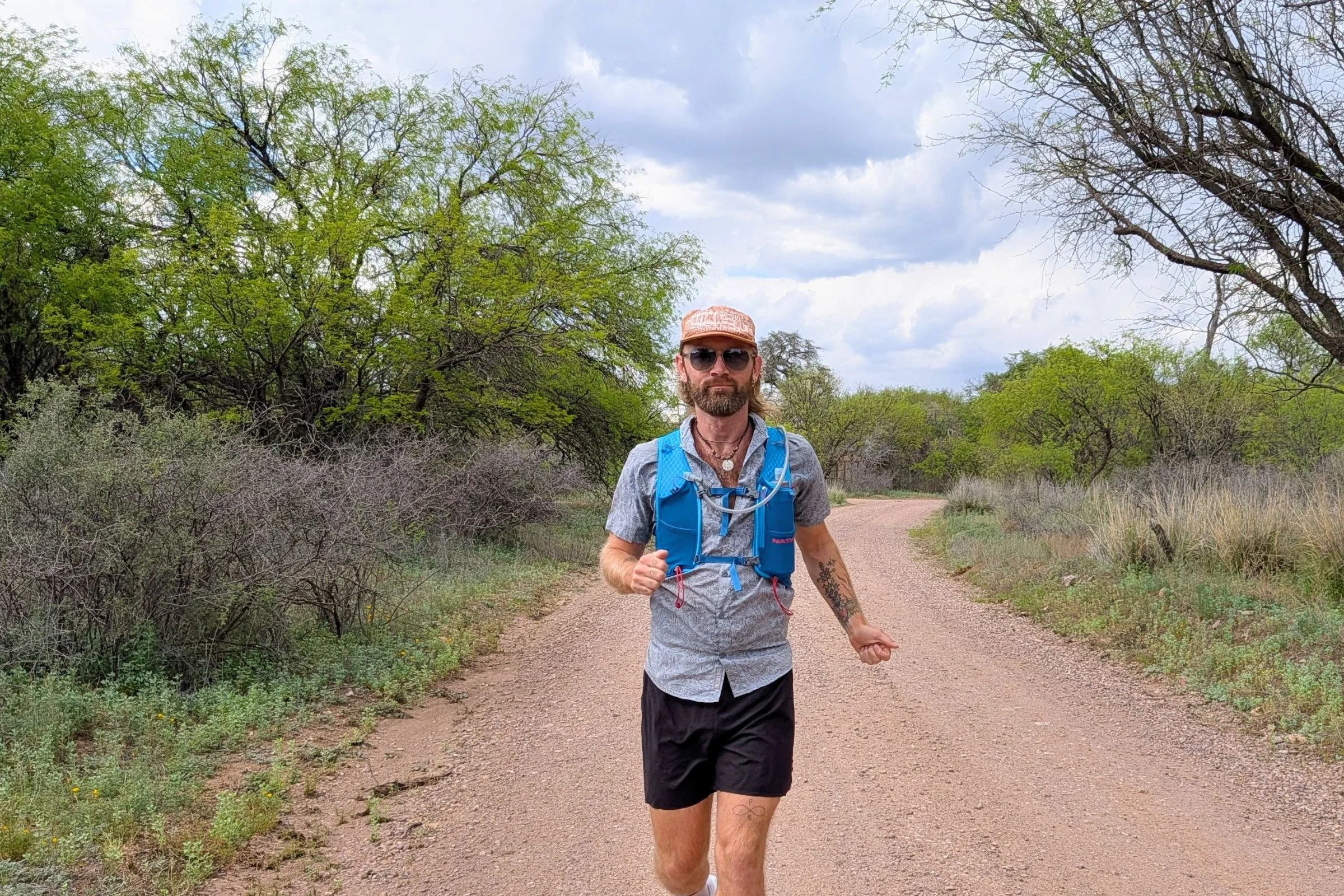 Man jogging along a dirt road through open terrain, wearing a Nathan VaporAir