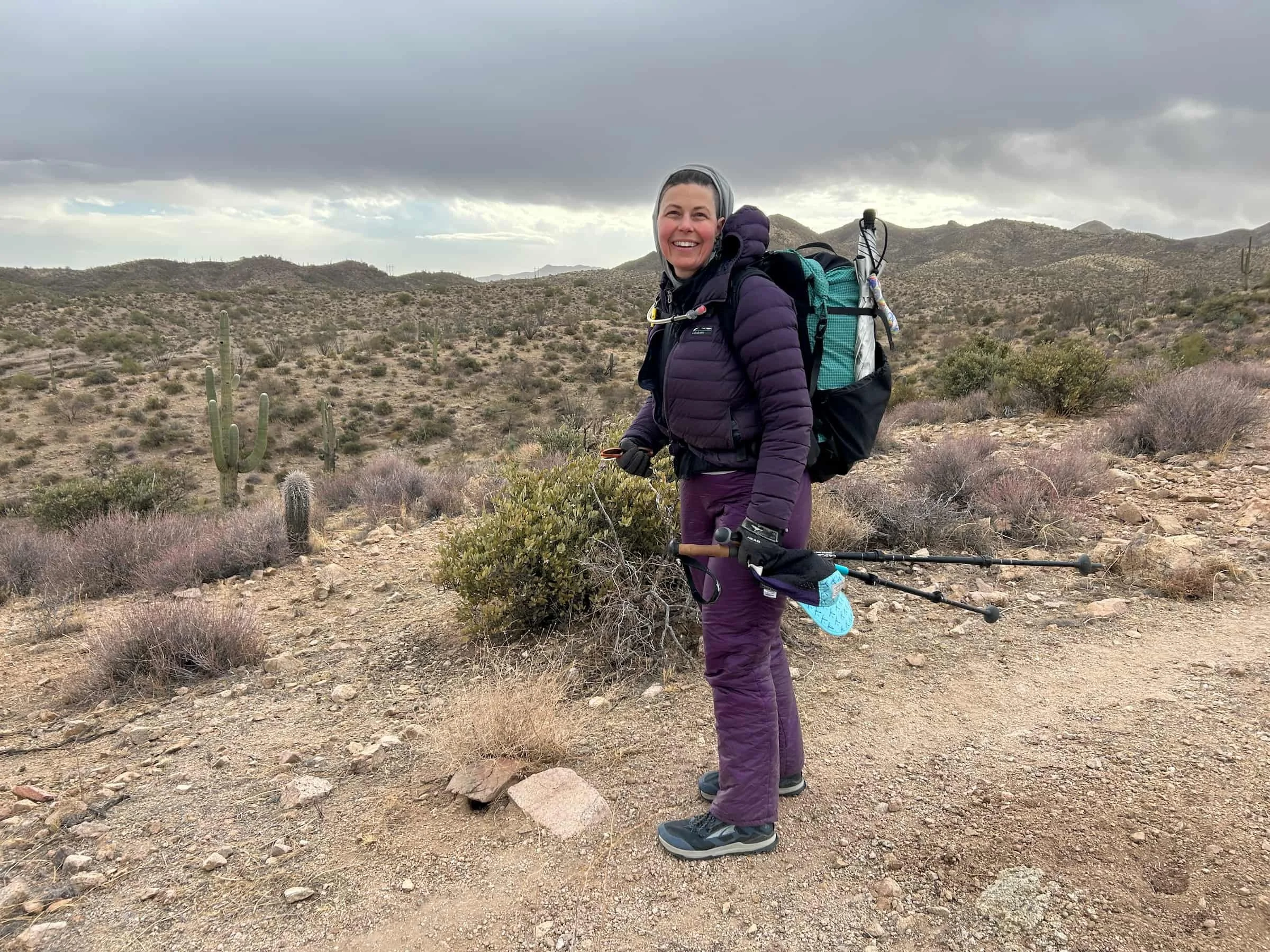 a woman in purple puffy pants in a cold looking desert with a storm coming on