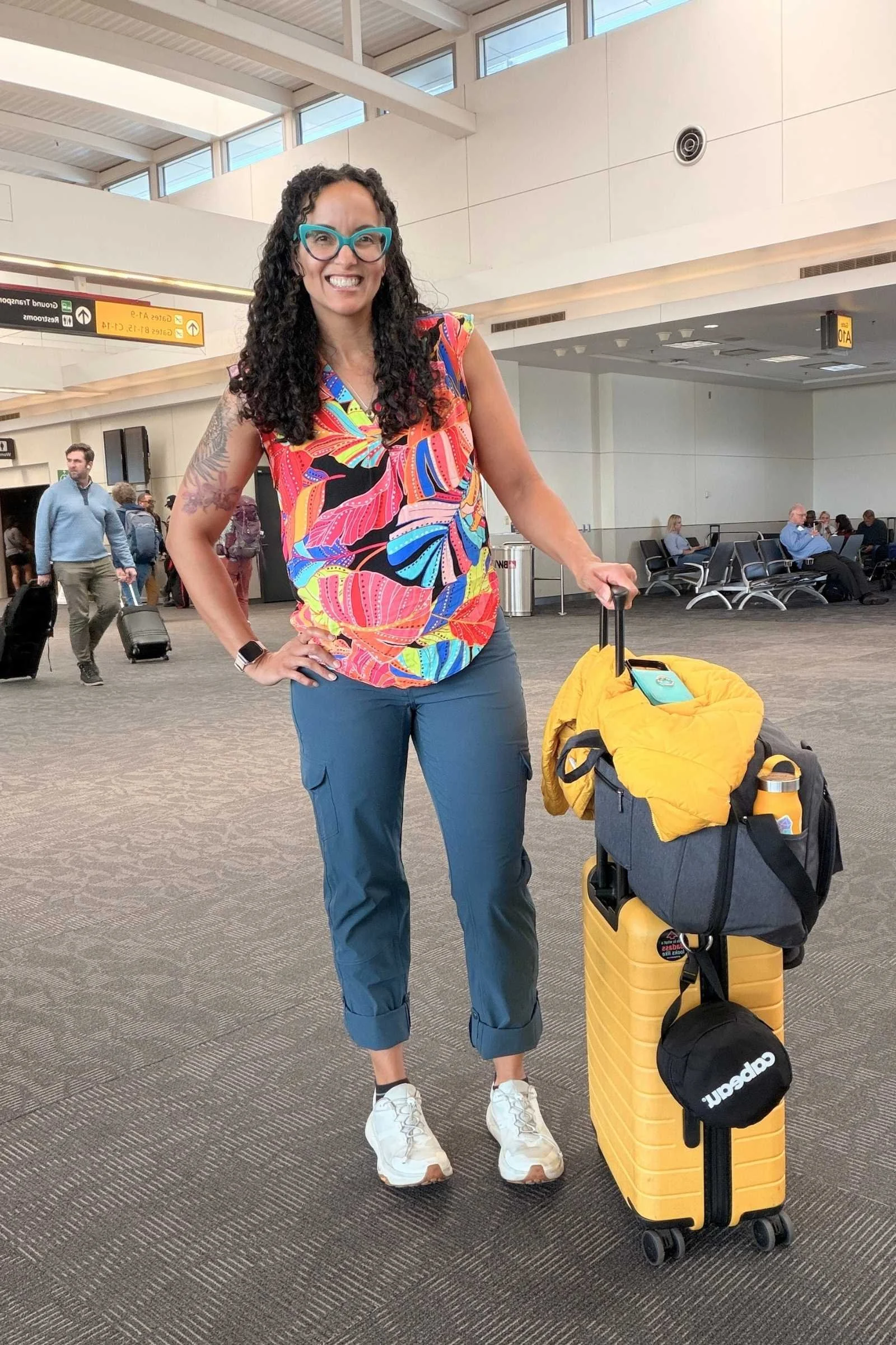 Woman wearing Kuhl Freeflex Roll Up Pant travel pants in dark teal blue in an airport