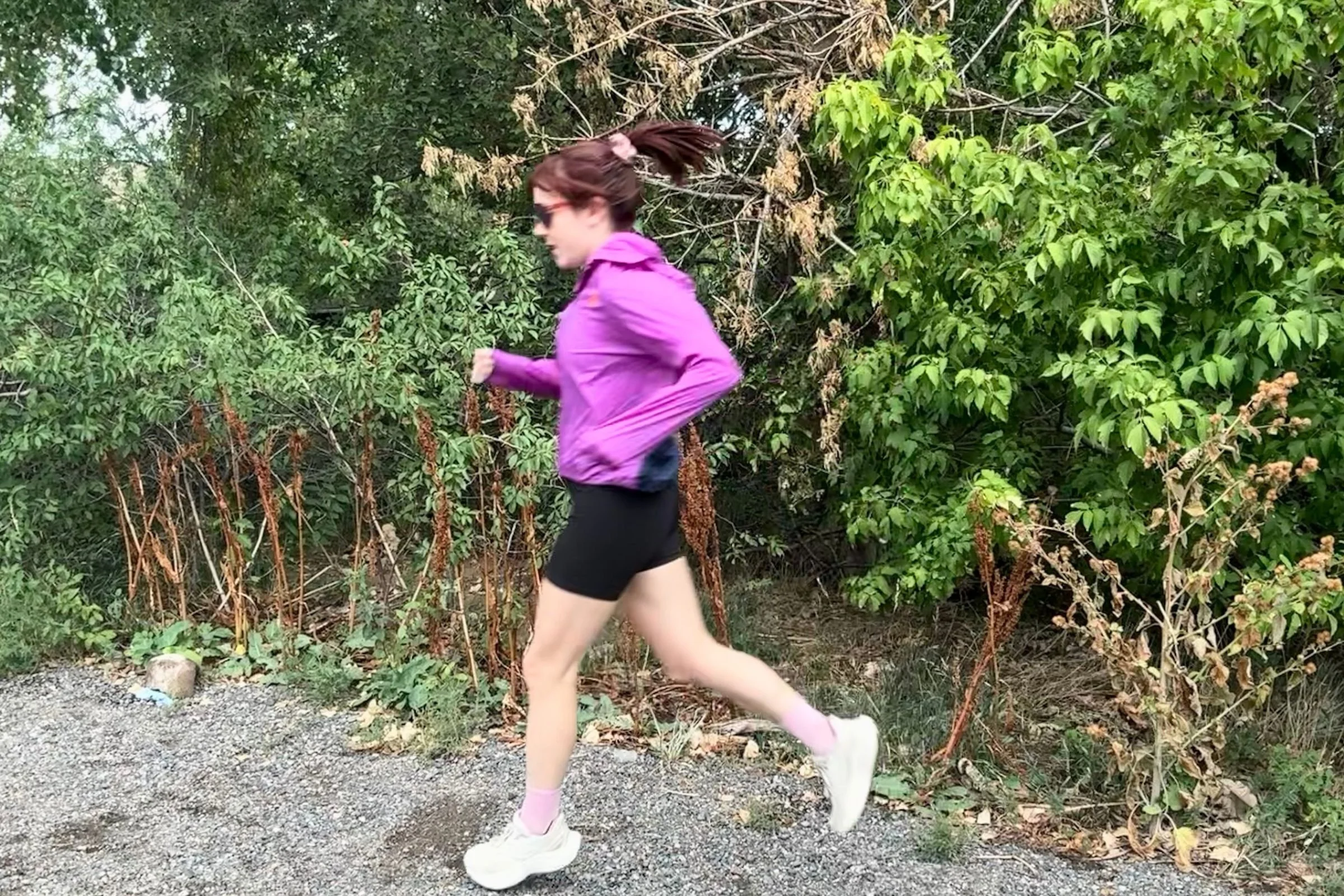 A woman in a purple jacket and black shorts running in the Saucony Triumph 24 Road Running Shoe.