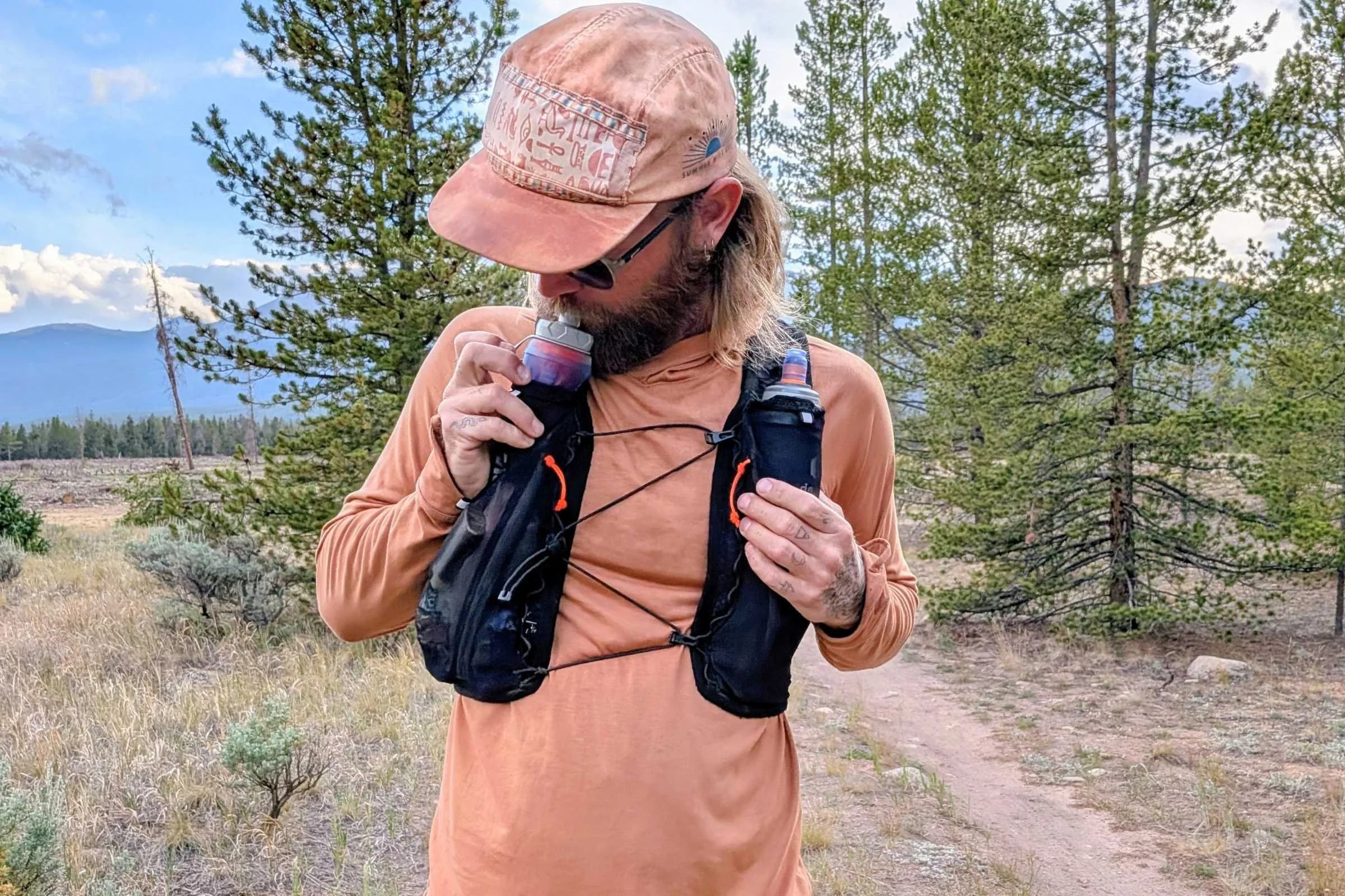 A person wearing Hyperlite Mountain Gear Pemi 15 Running Vest with two water bottles drinks