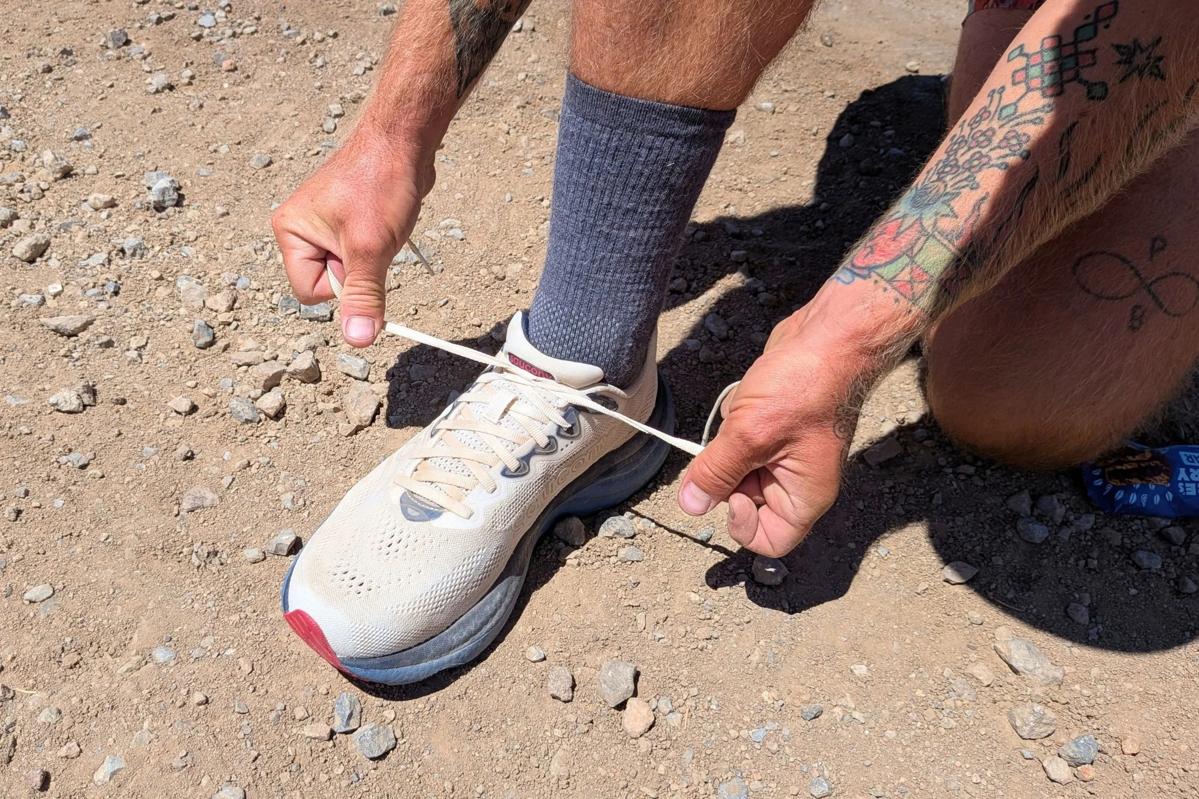 A person ties a Saucony Ride 19 Road Running Shoe on a dirt trail.