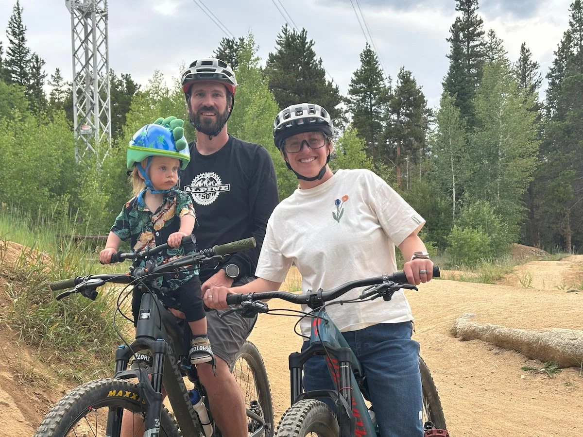 The author and another tester, who is holding a toddler, both on mountain bikes.