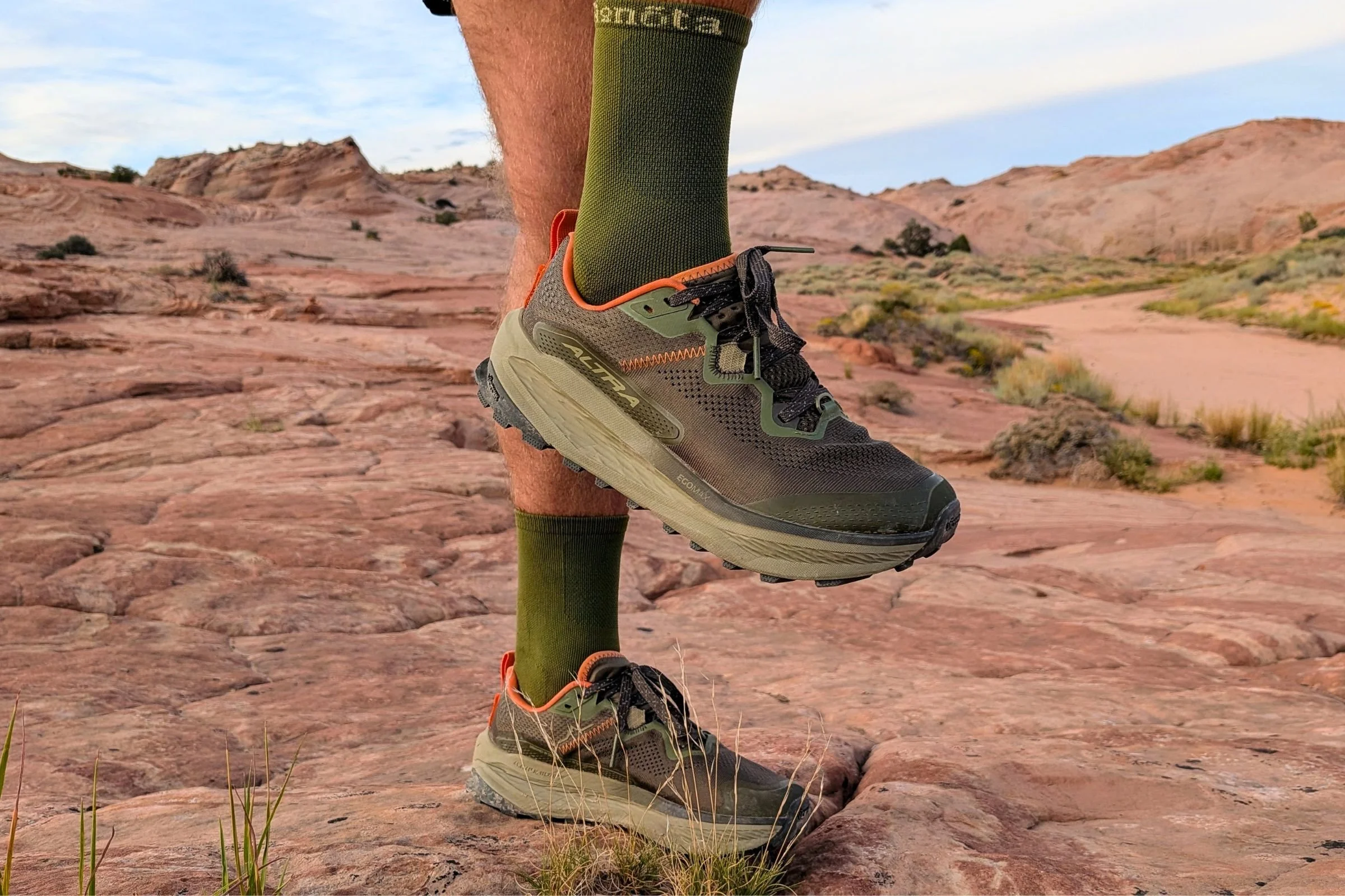 A person wearing the Altra Olympus 7 stands on a rock in a natural landscape.