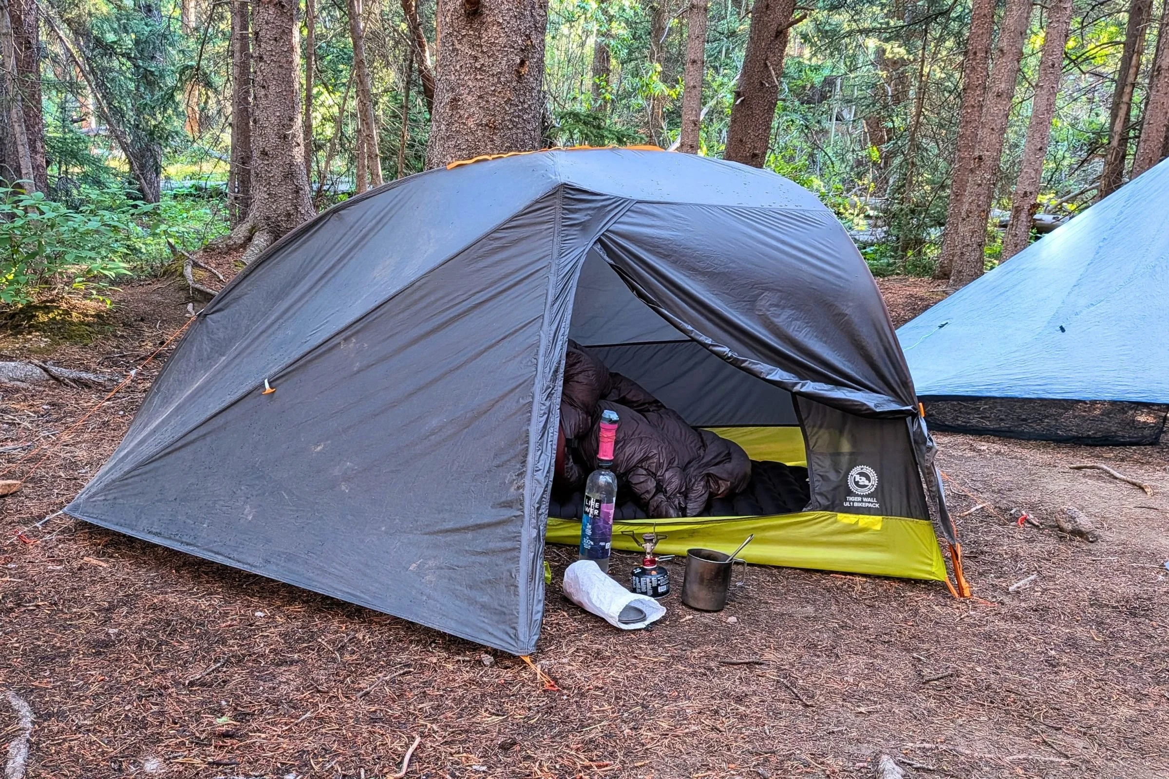 The Big Agnes Tiger Wall UL1 Bikepack Tent with a sleeping quilt inside and a forest backdrop.