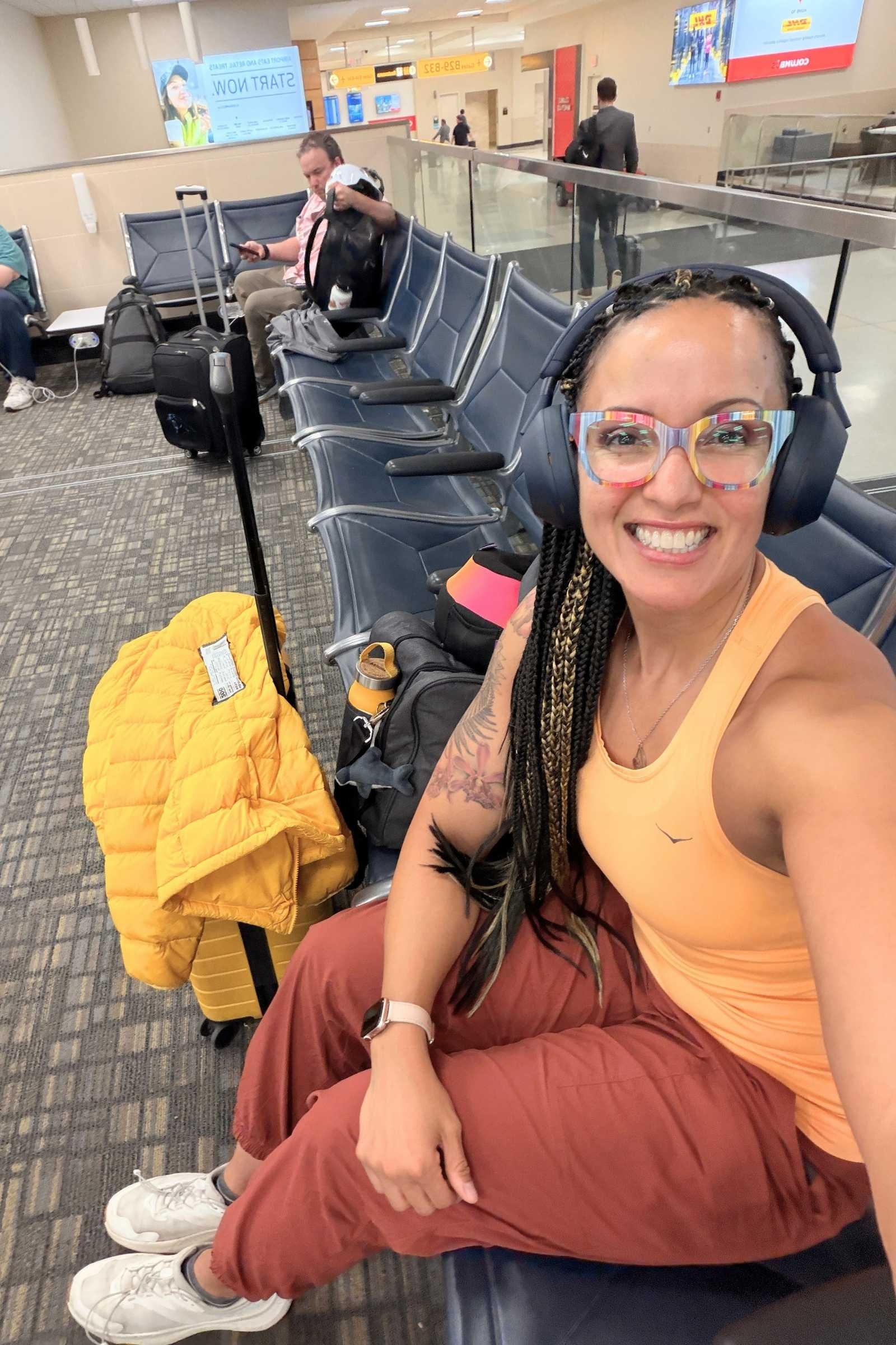 Woman wearing REI Co-op Trailmade Relax travel pants in brick red color sitting in chair in an airport