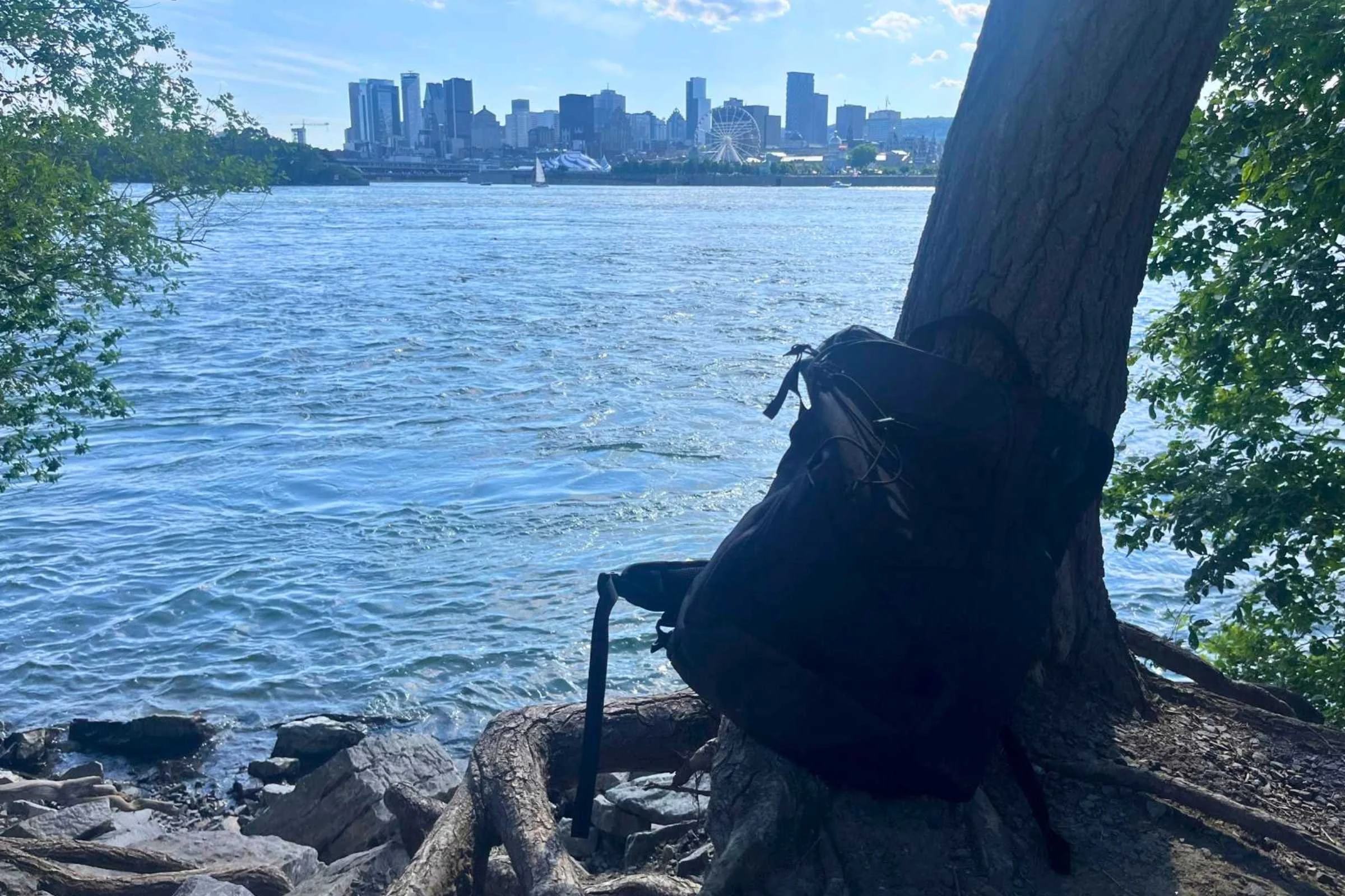 ULA Ultra Dragonfly 30L Adventure Travel Backpack on the ground beside a tree at the edge of a lake.