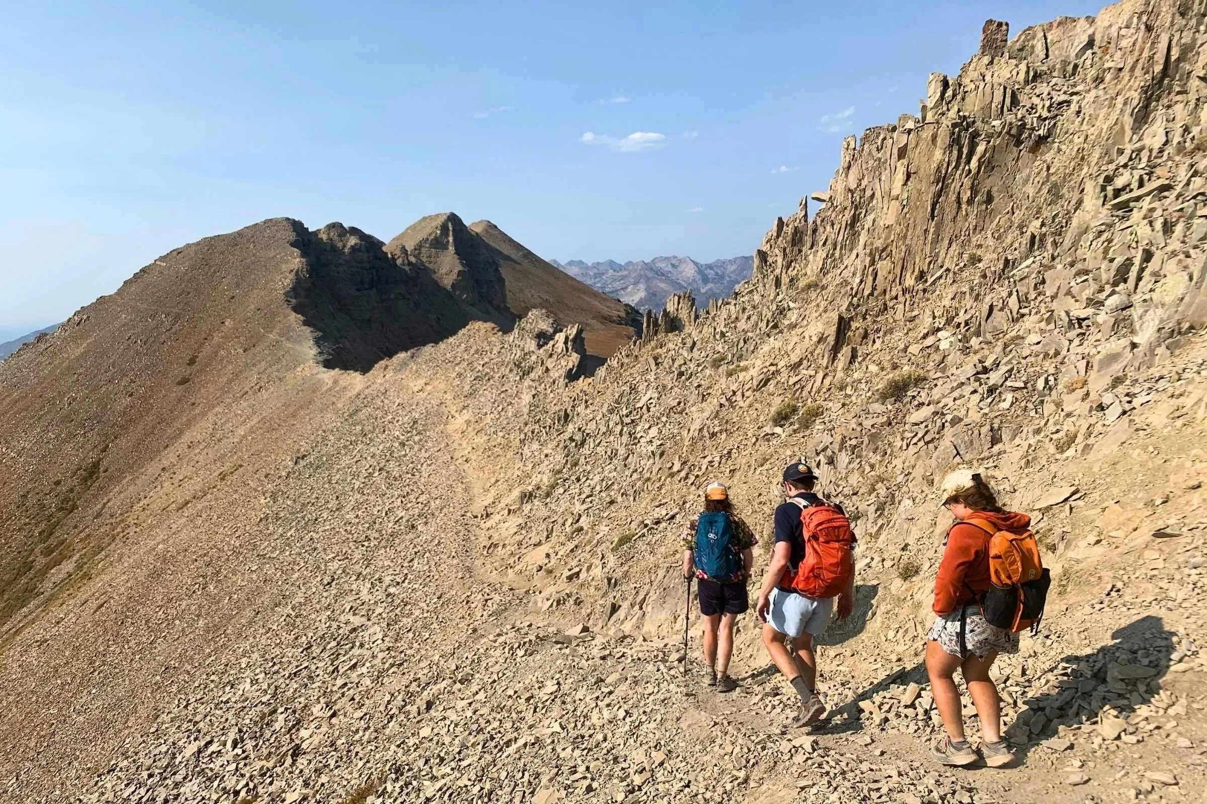 Three people wearing daypacks hiking above the treeline