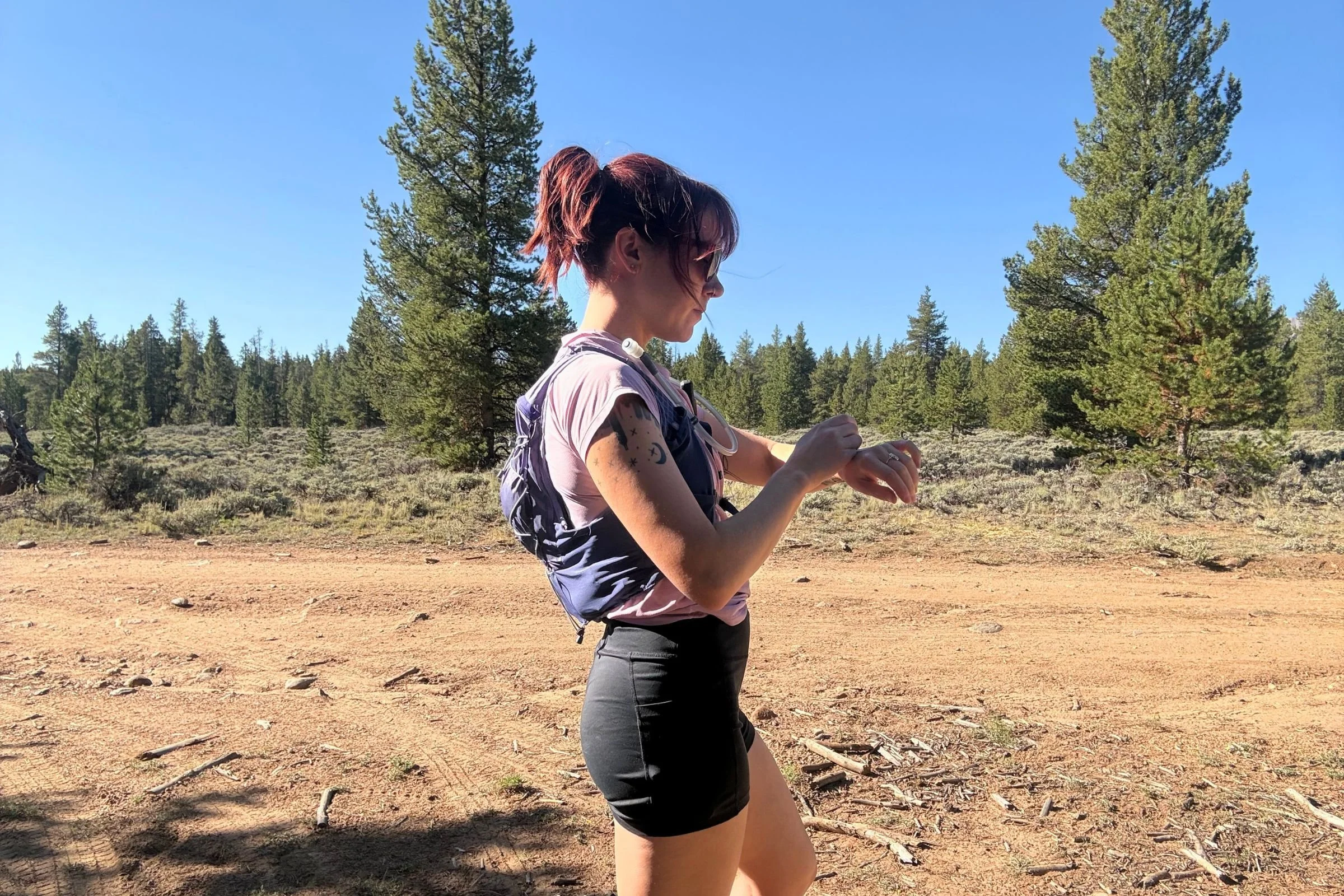 Woman standing side-on on a dirt road, wearing a Nathan VaporAir pack with athletic clothing.