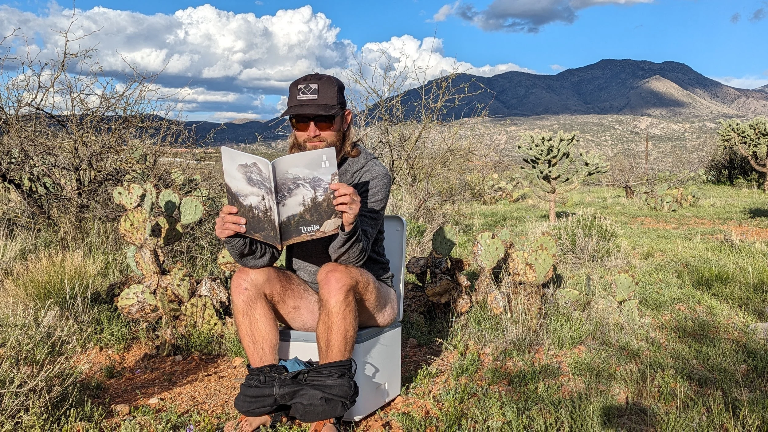 man sitting outside on compostable toilet reading magazine