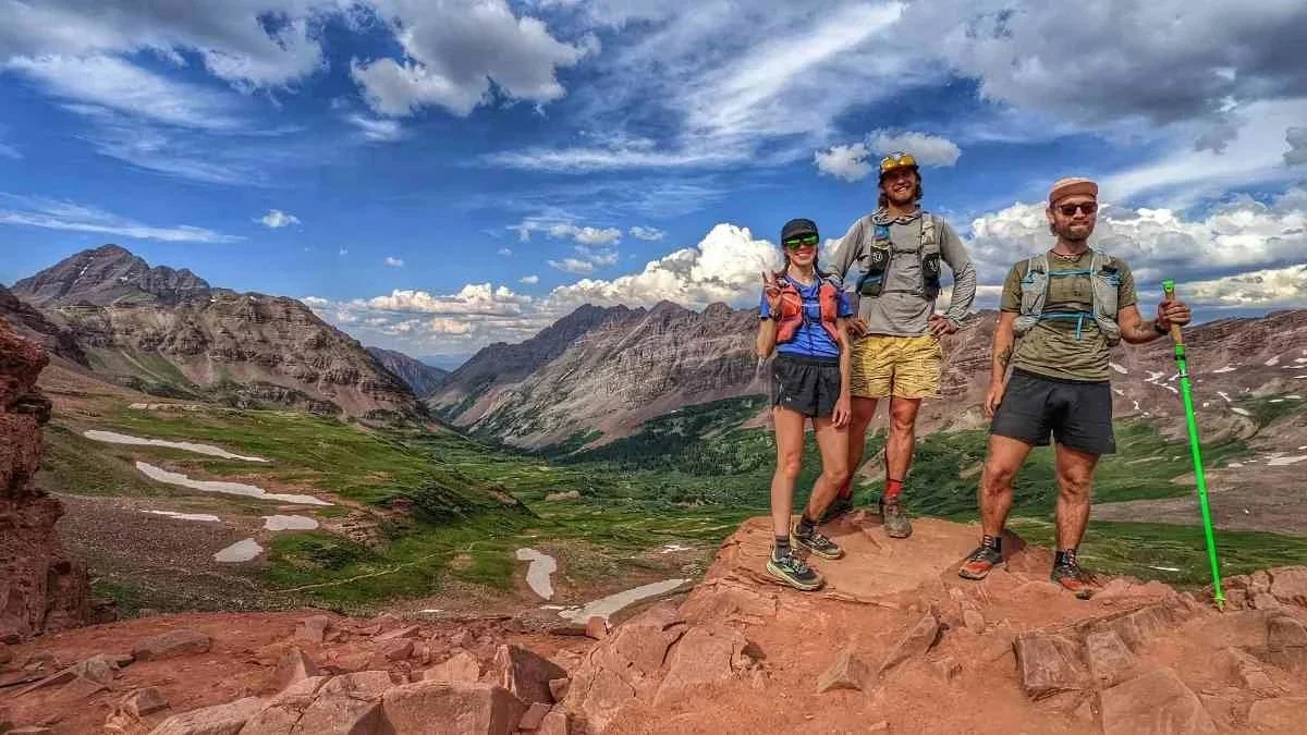 Three hikers standing on a red rock outcropping with magestic mountains in the background