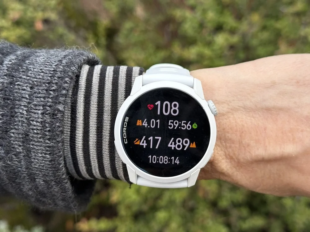 Woman wearing the COROS Pace 4 GPS watch with green foliage in the background.