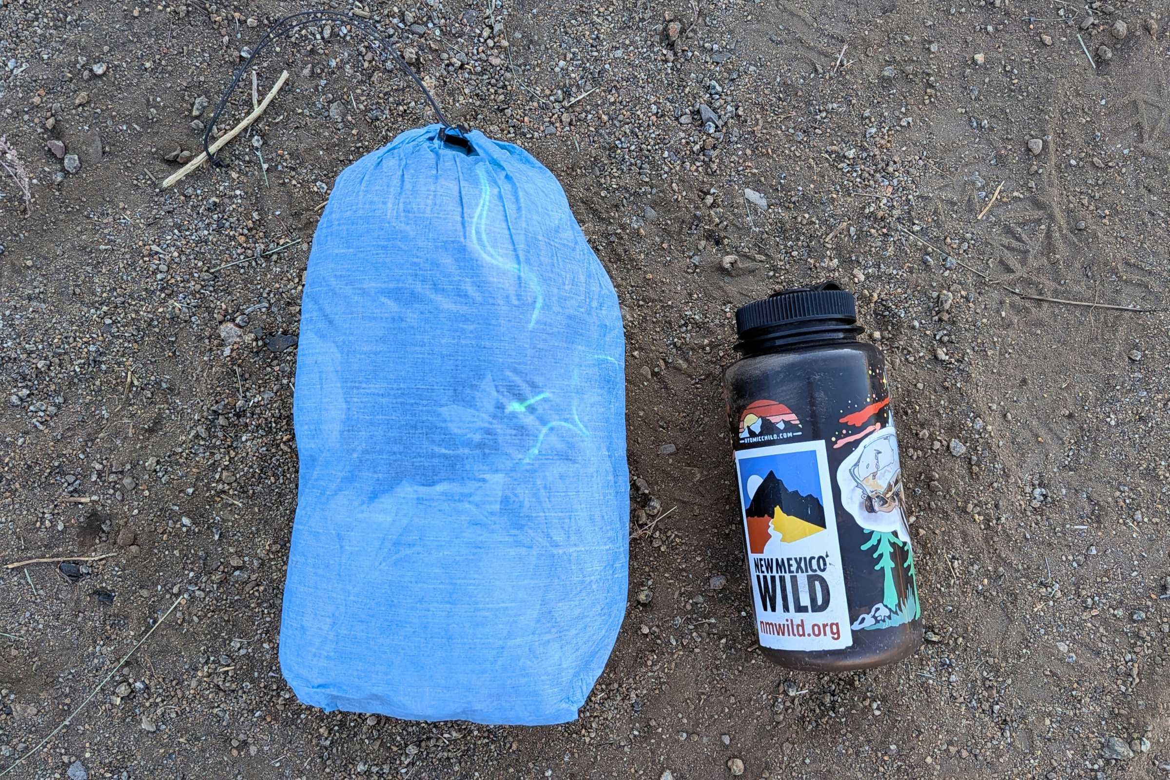 Water bottle and sleeping bag on the ground near a Zpacks Hexamid Ultralight Tent setup.