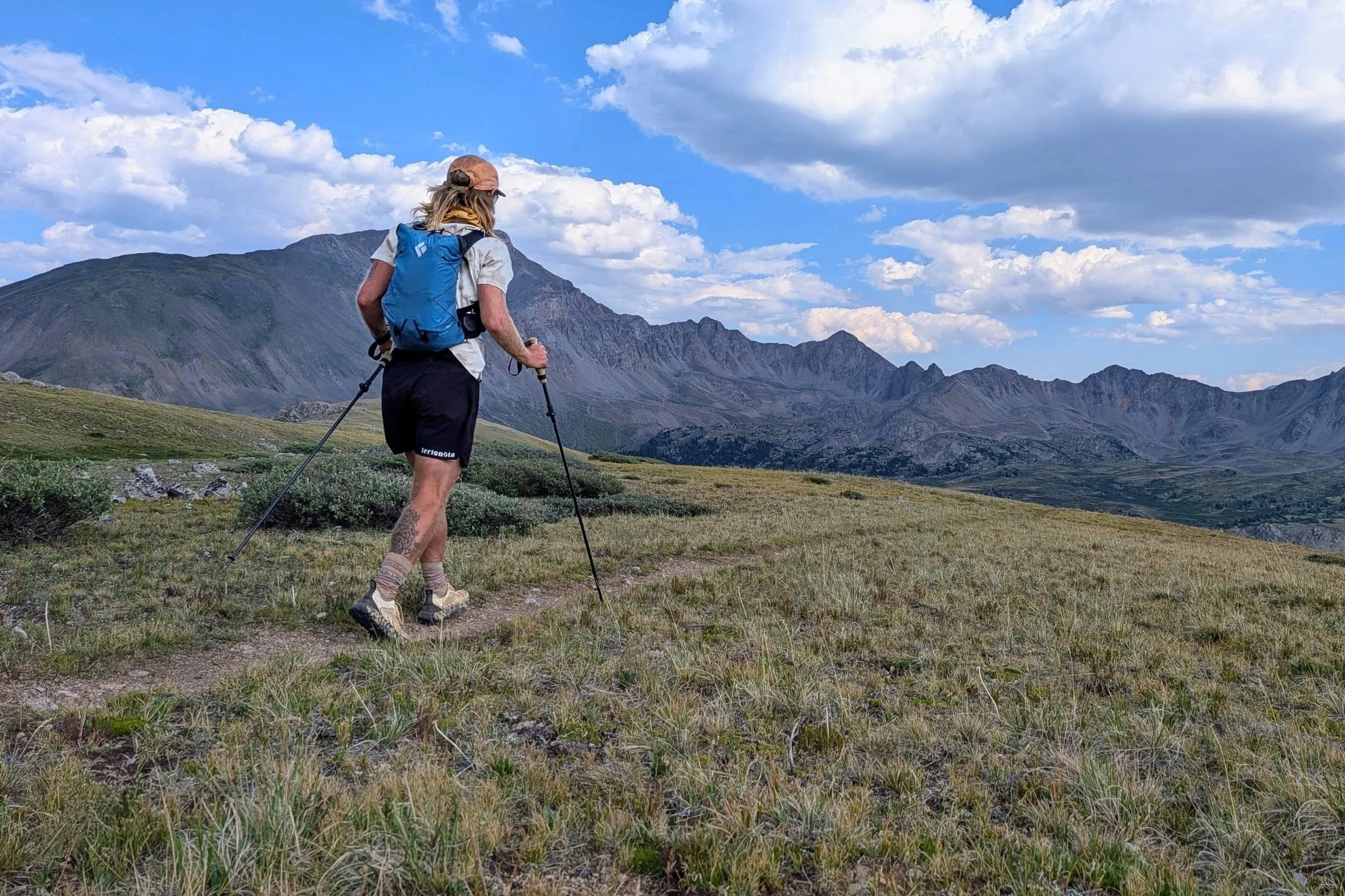 A man with hiking poles wears the Black Diamond Distance 15 Backpack on a trail.