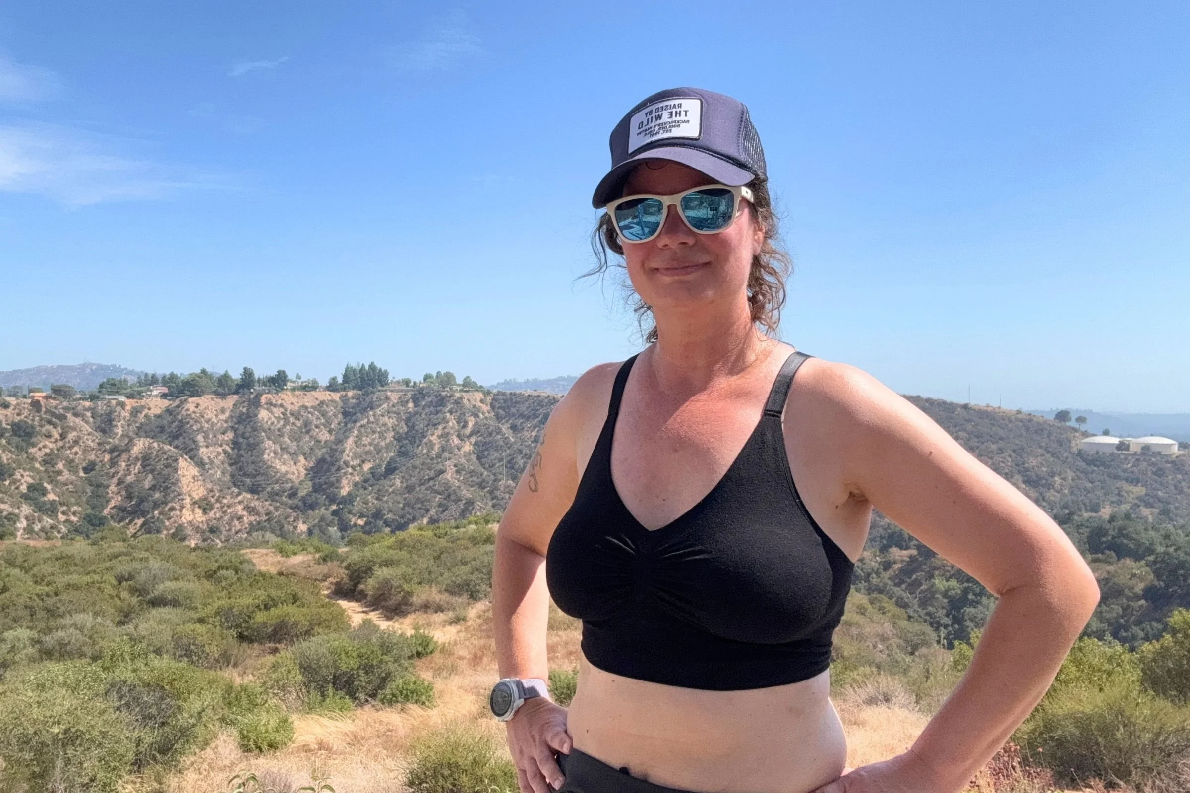 The author wearing the black BRANWYN Essential Supreme Bra in medium, with the optional pads inserted. Hills and trees are in the background.