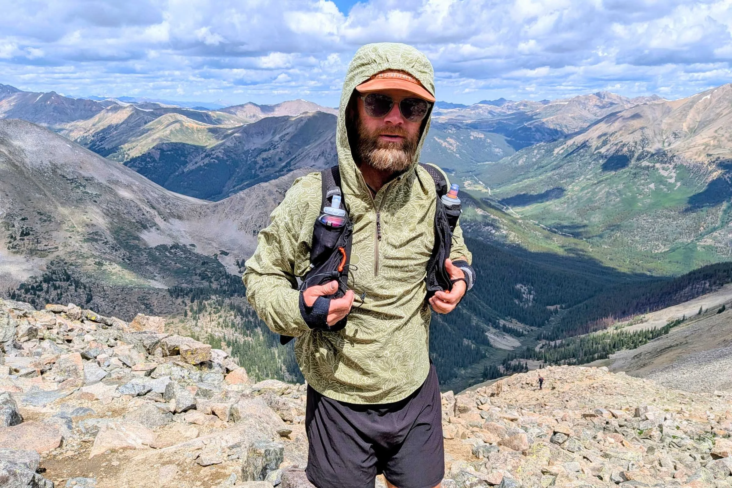 Hyperlite Mountain Gear Pemi 15 Running Vest shown on a trail runner standing on a rocky summit with mountain views in the background