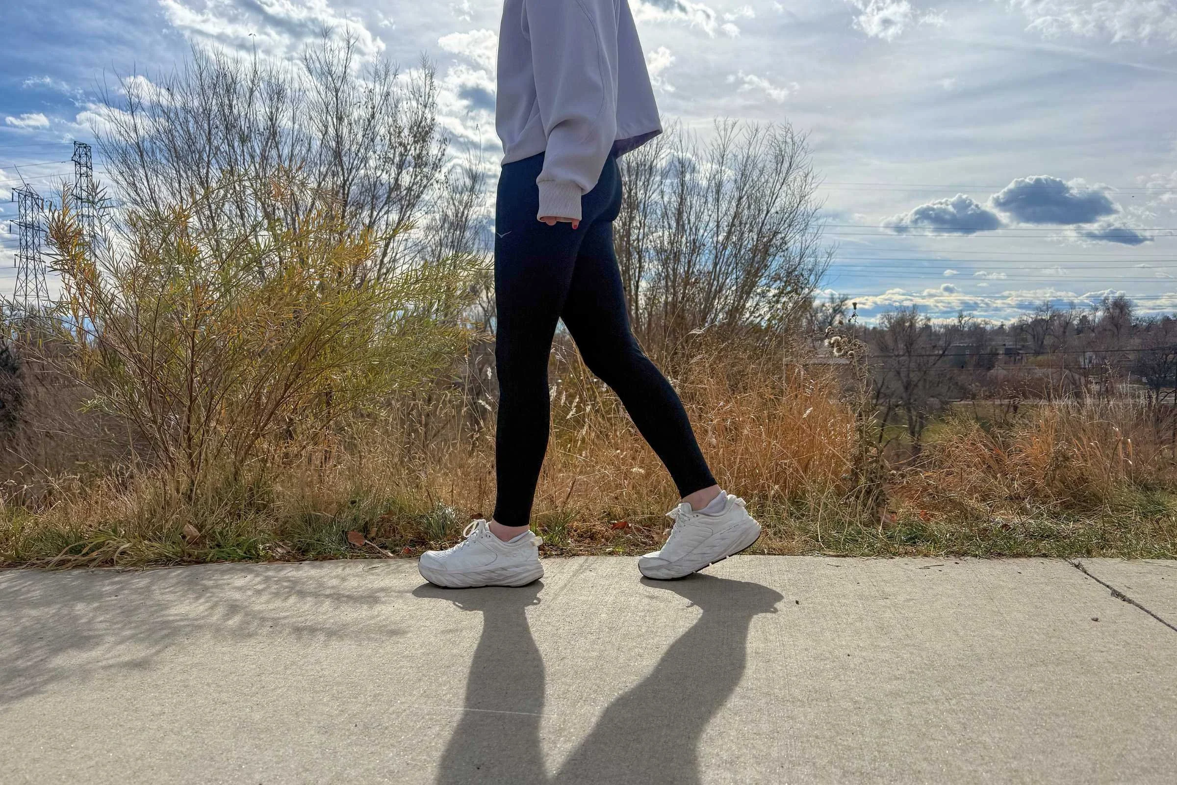 side profile of a woman walking on bike path in white hoka bondi sr shoes