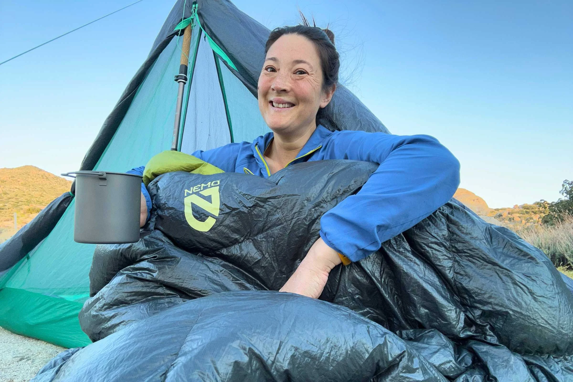 Camper sitting in Big Agnes String Ridge VST tent wrapped in sleeping bag with coffee mug