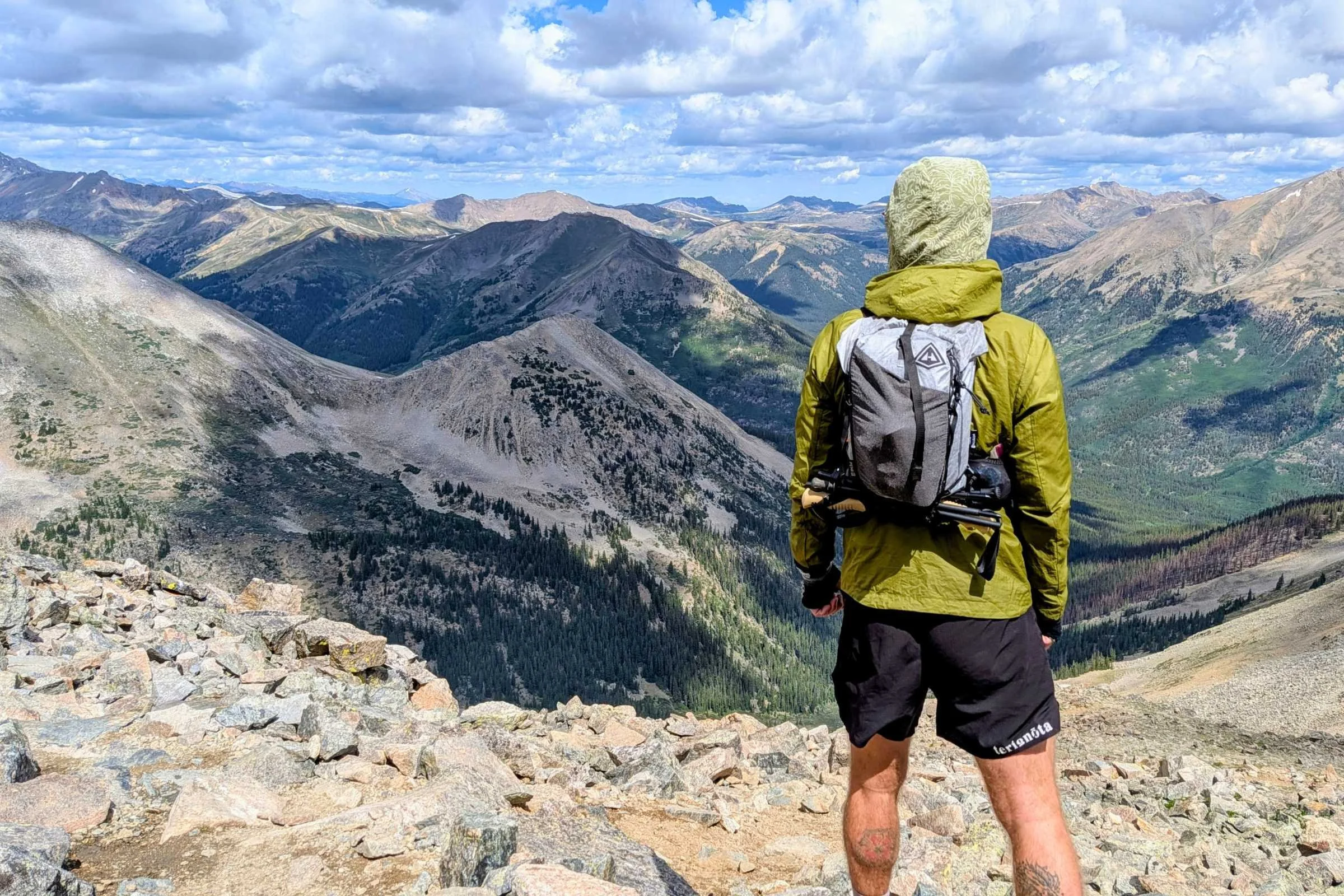 Hyperlite Mountain Gear Pemi 15 Running Vest shown on a trail runner standing on a rocky summit with mountain views in the background