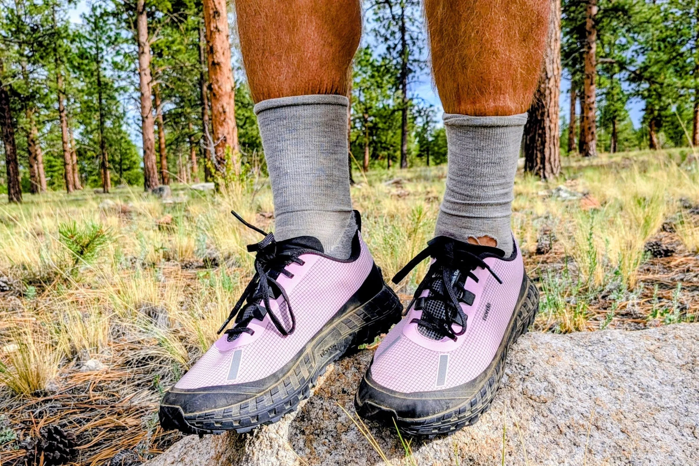 Man wearing pink Norda 000 Trail Running Shoes standing on a rock in the woods.