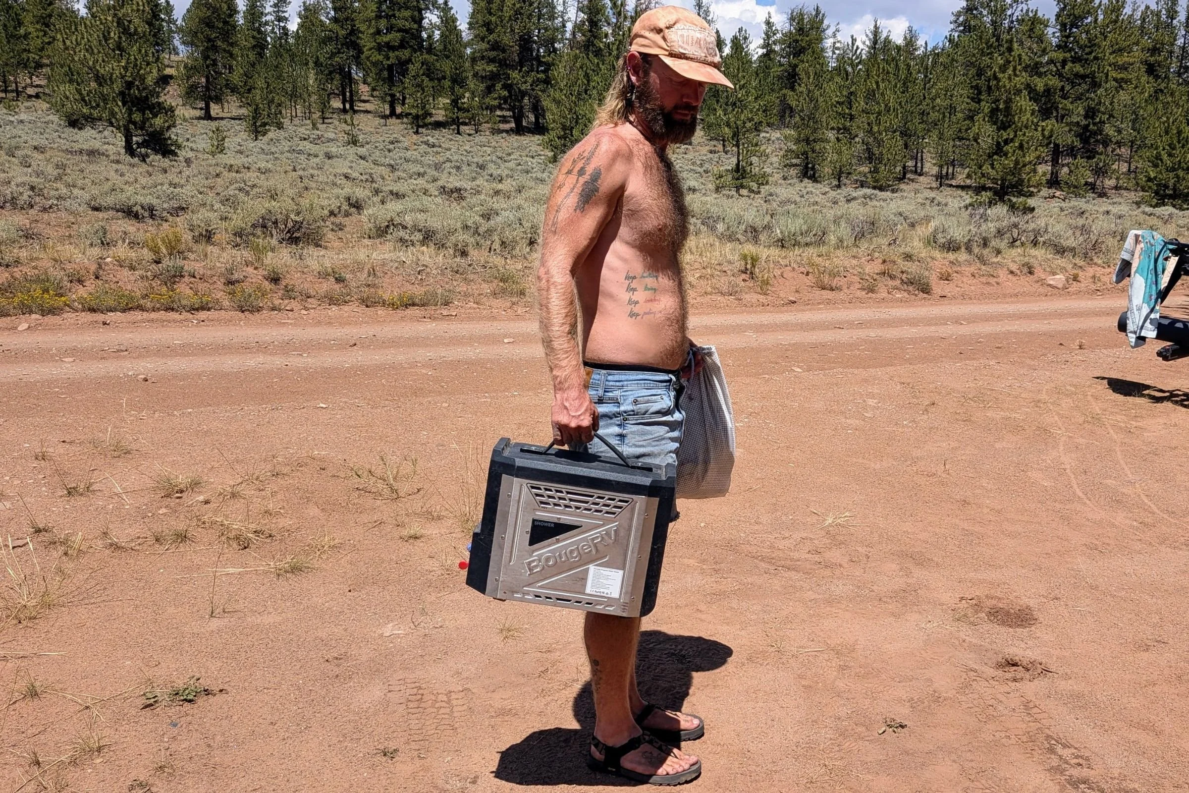 Man carrying the BougeRV portable water heater on a red clay road in Utah