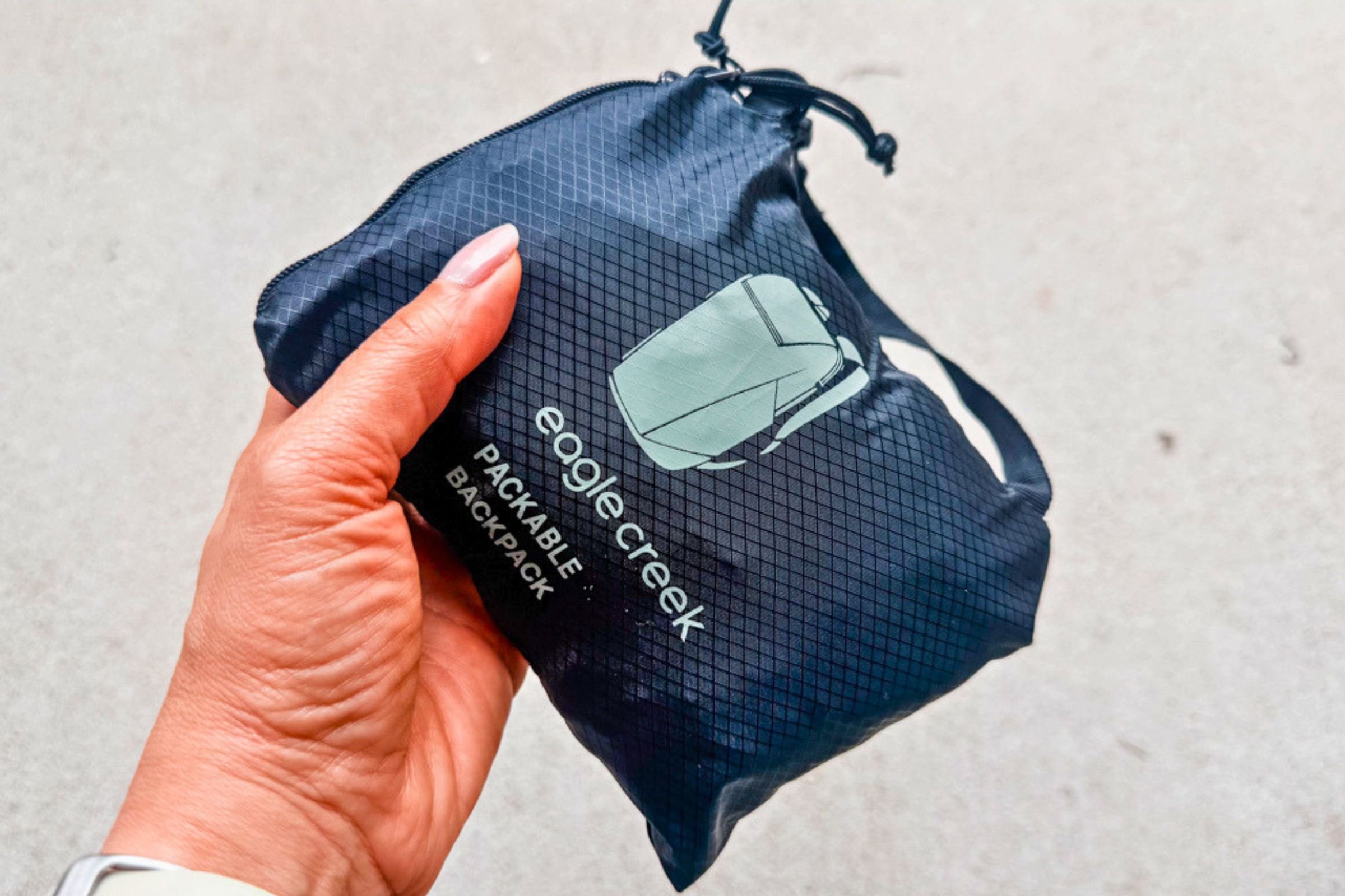 Hand holding a compact, packed black Eagle Creek Packable Backpack