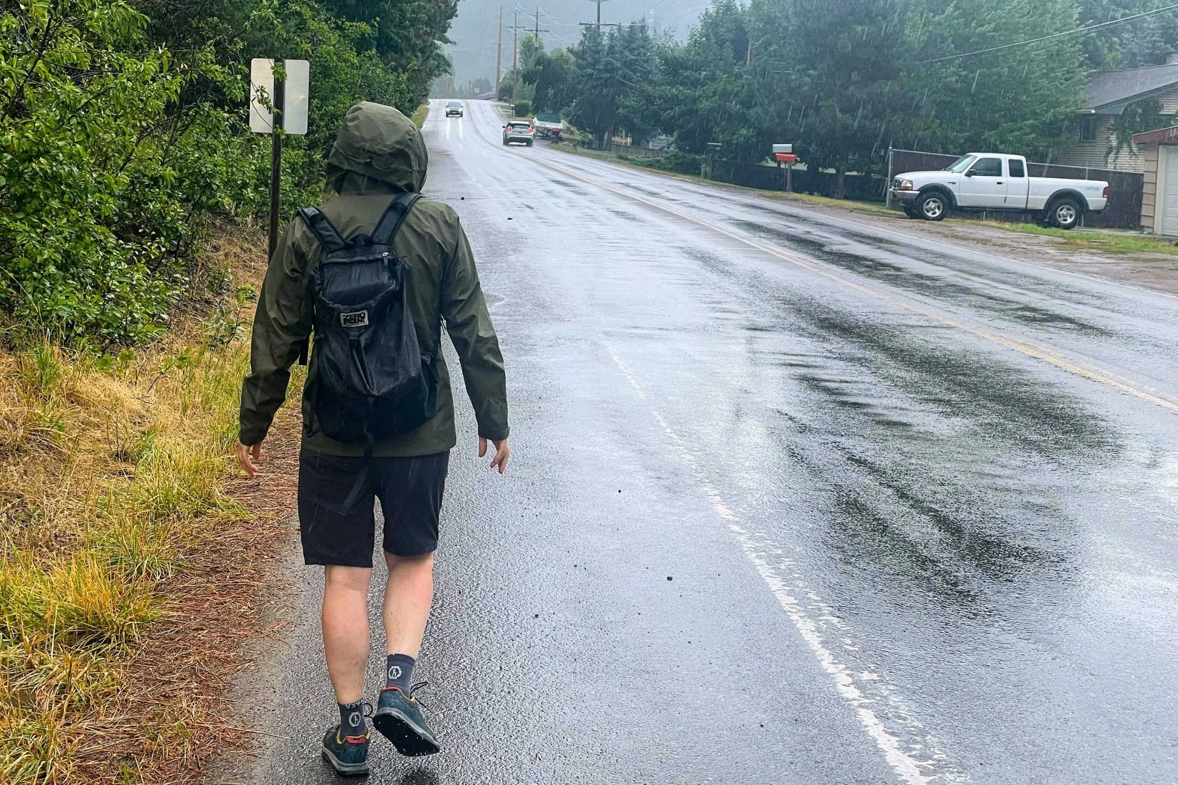 HIker walking down the side of a road in the rain wearing the Arc'teryx Beta SL Rain Jacket