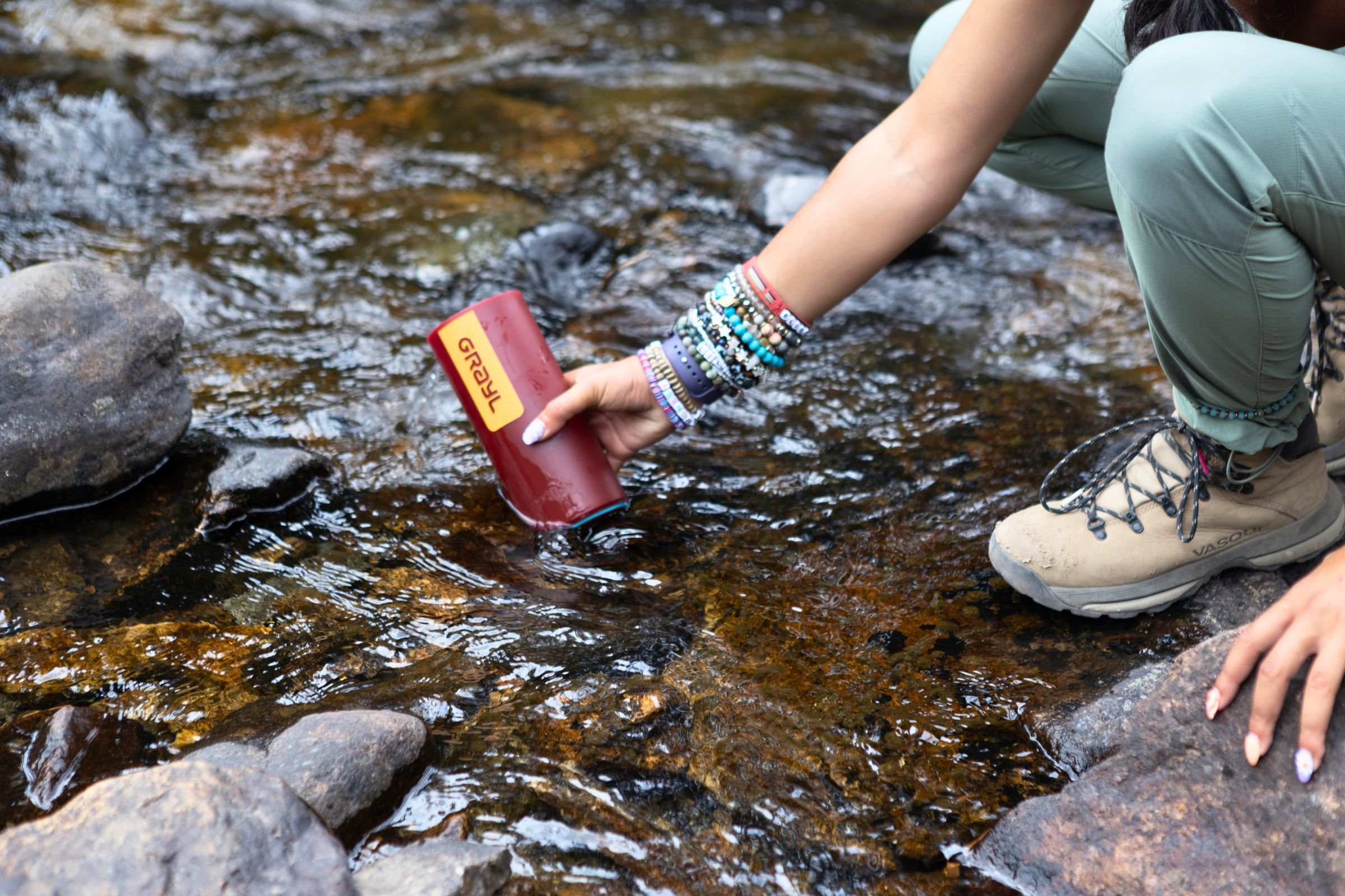 A person holding a red Grayl GeoPress Purifier in a stream.