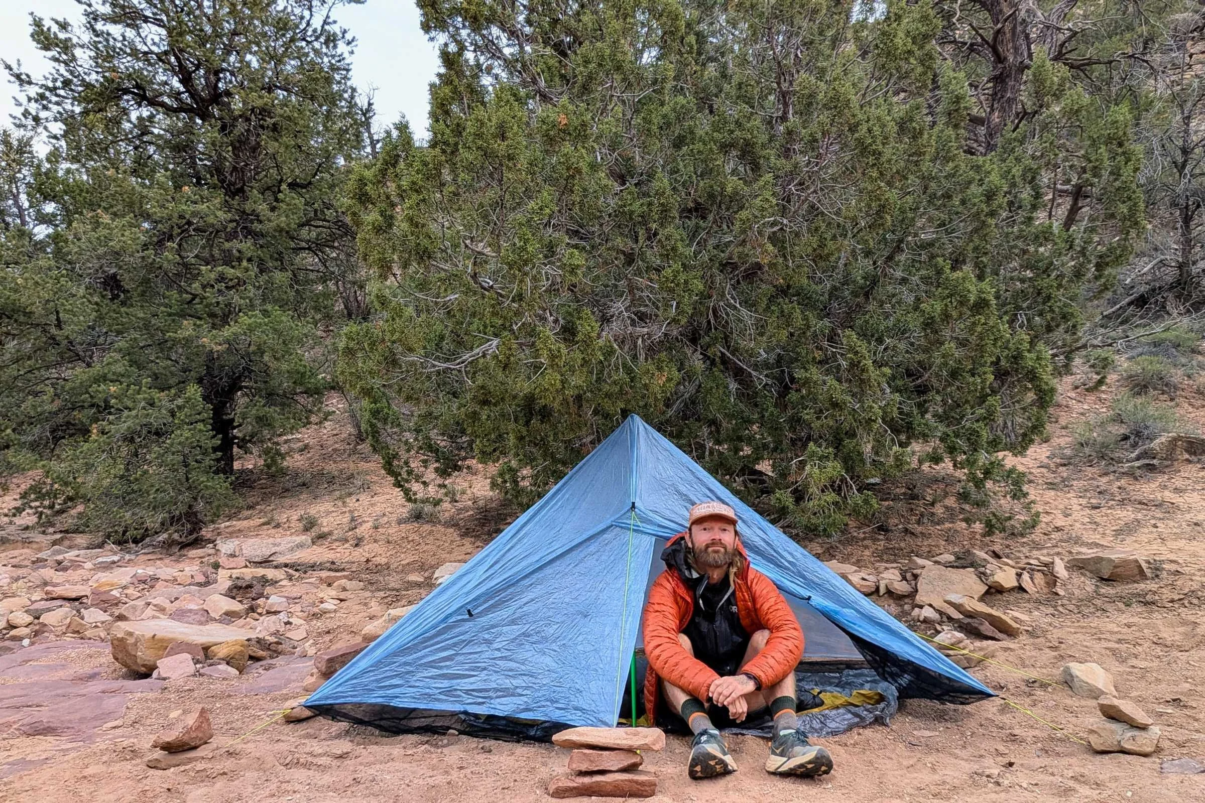 Man sitting in front of a Zpacks Hexamid Ultralight Tent in a desert campsite.