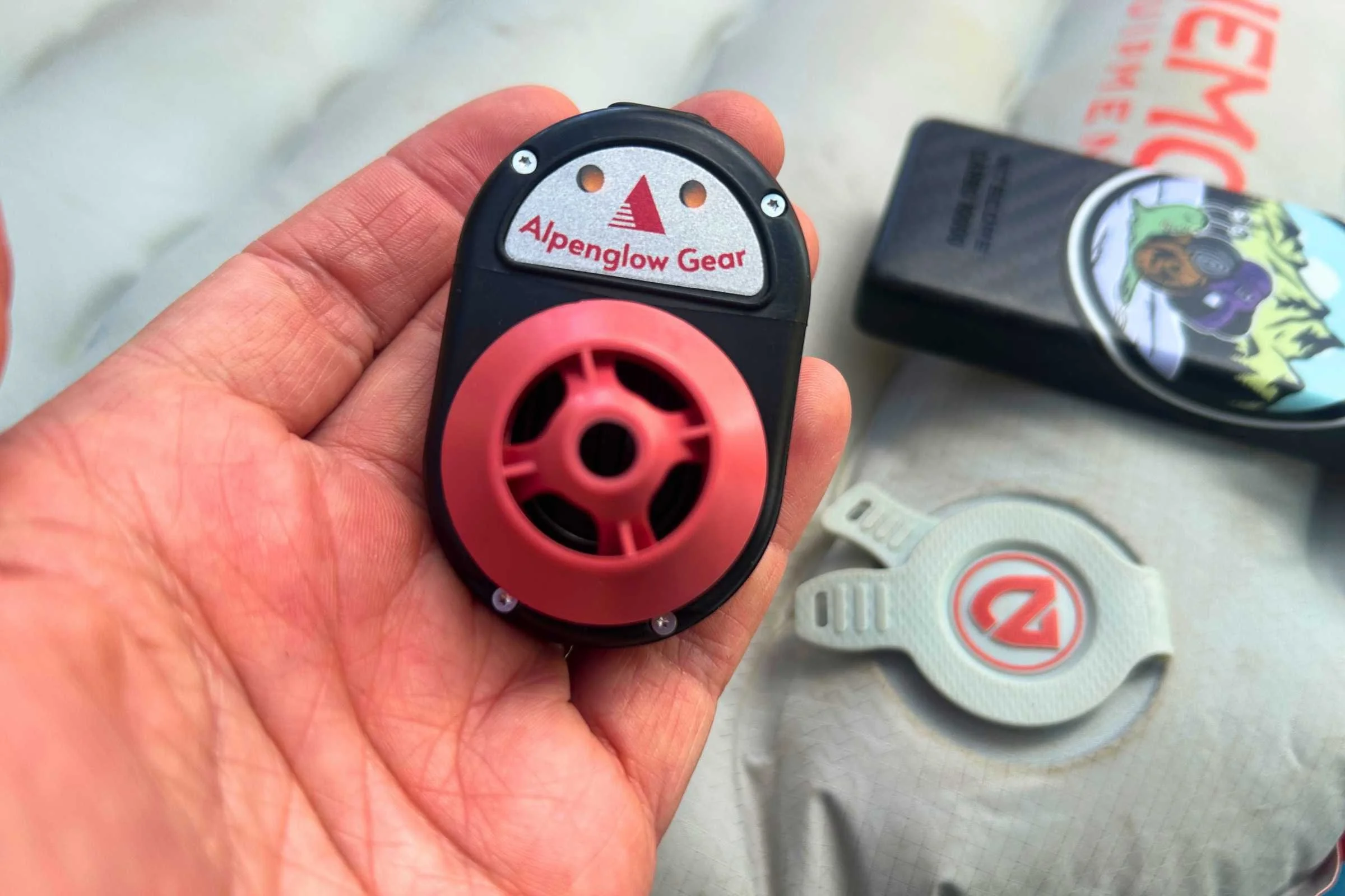 Alpenblow Lux remote control held in a person’s hand, showing the red and black device up close.