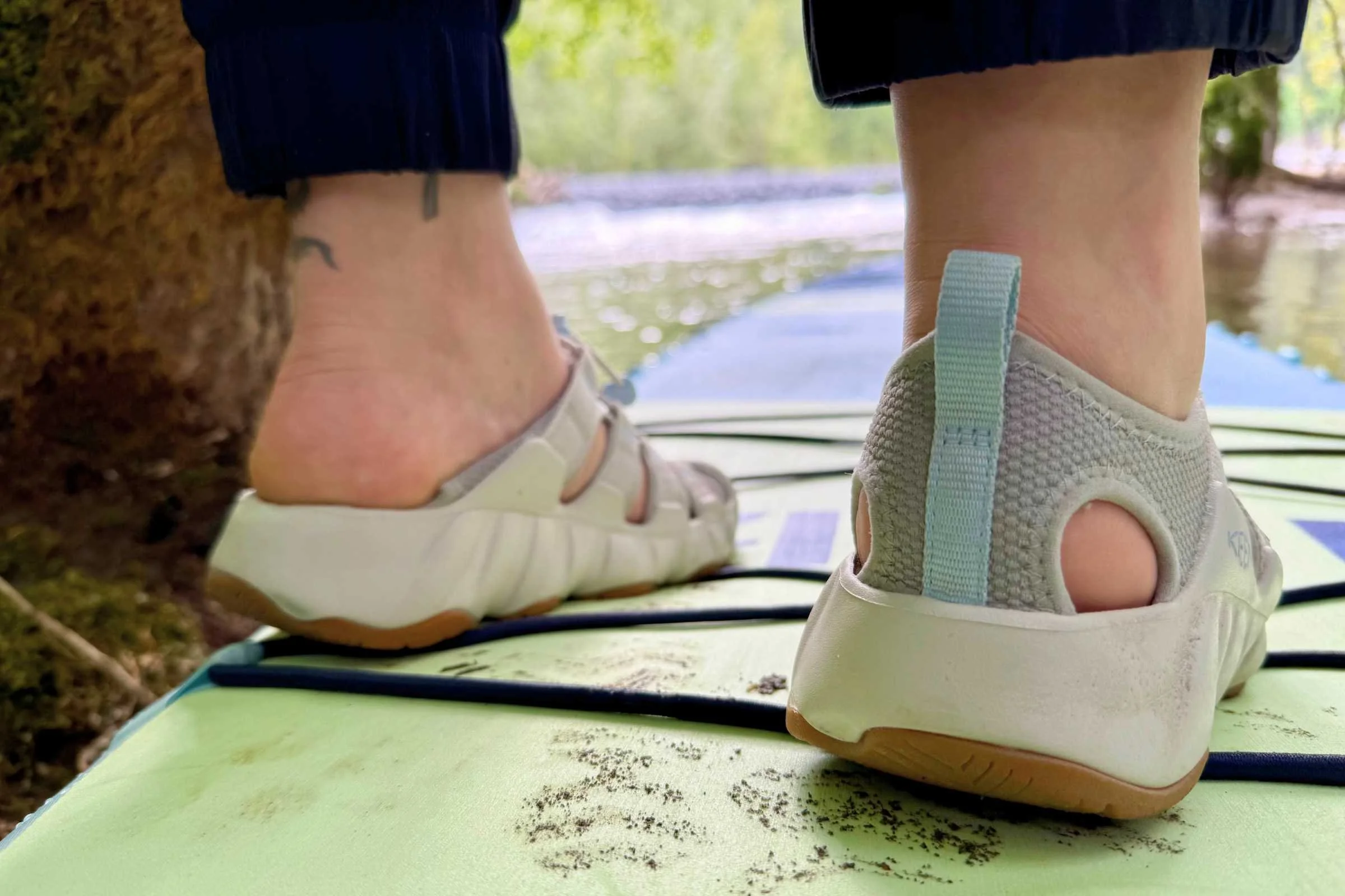Someone on a paddleboard wearing the Keen Hyperport H2 shoes with one foot showing how you can kick the back down and use the shoes as slides