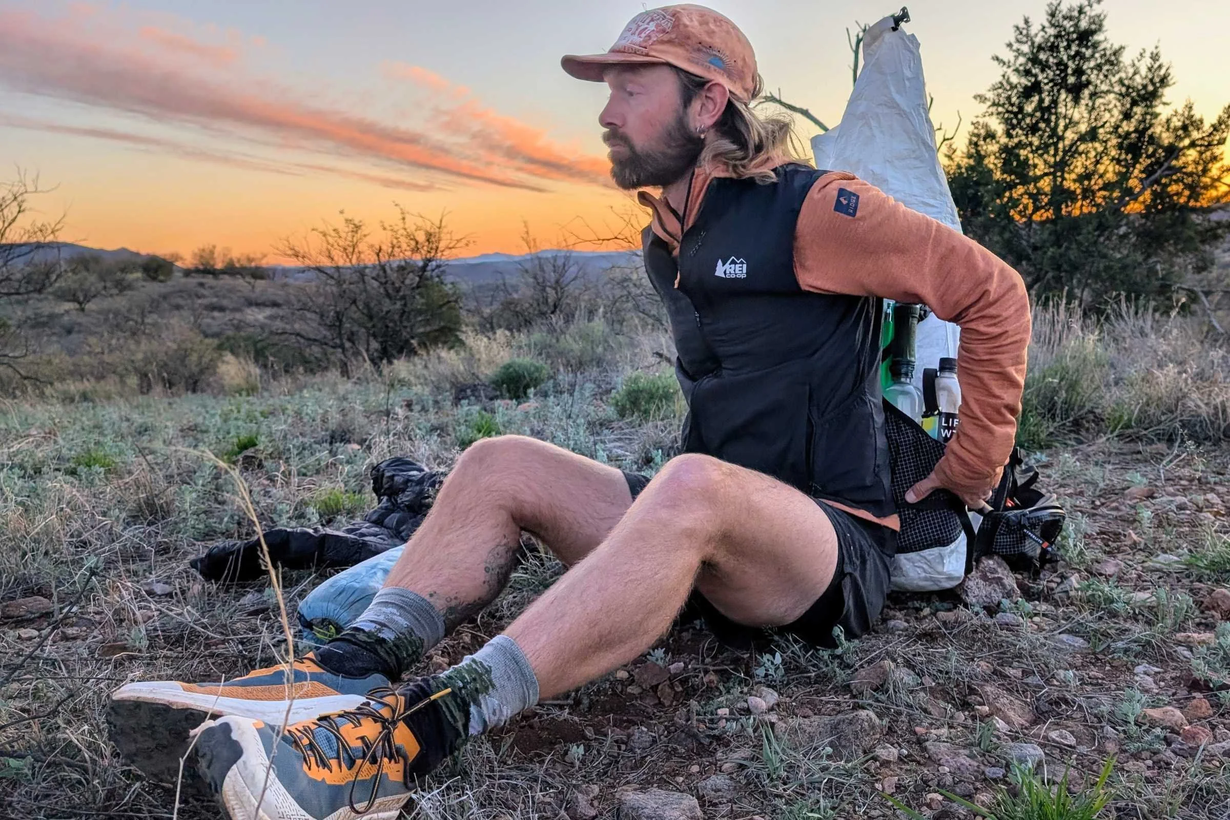 Man sitting on the ground at sunset wearing REI Co-op Swiftland running gear including the REI Swiftland Running Vest.