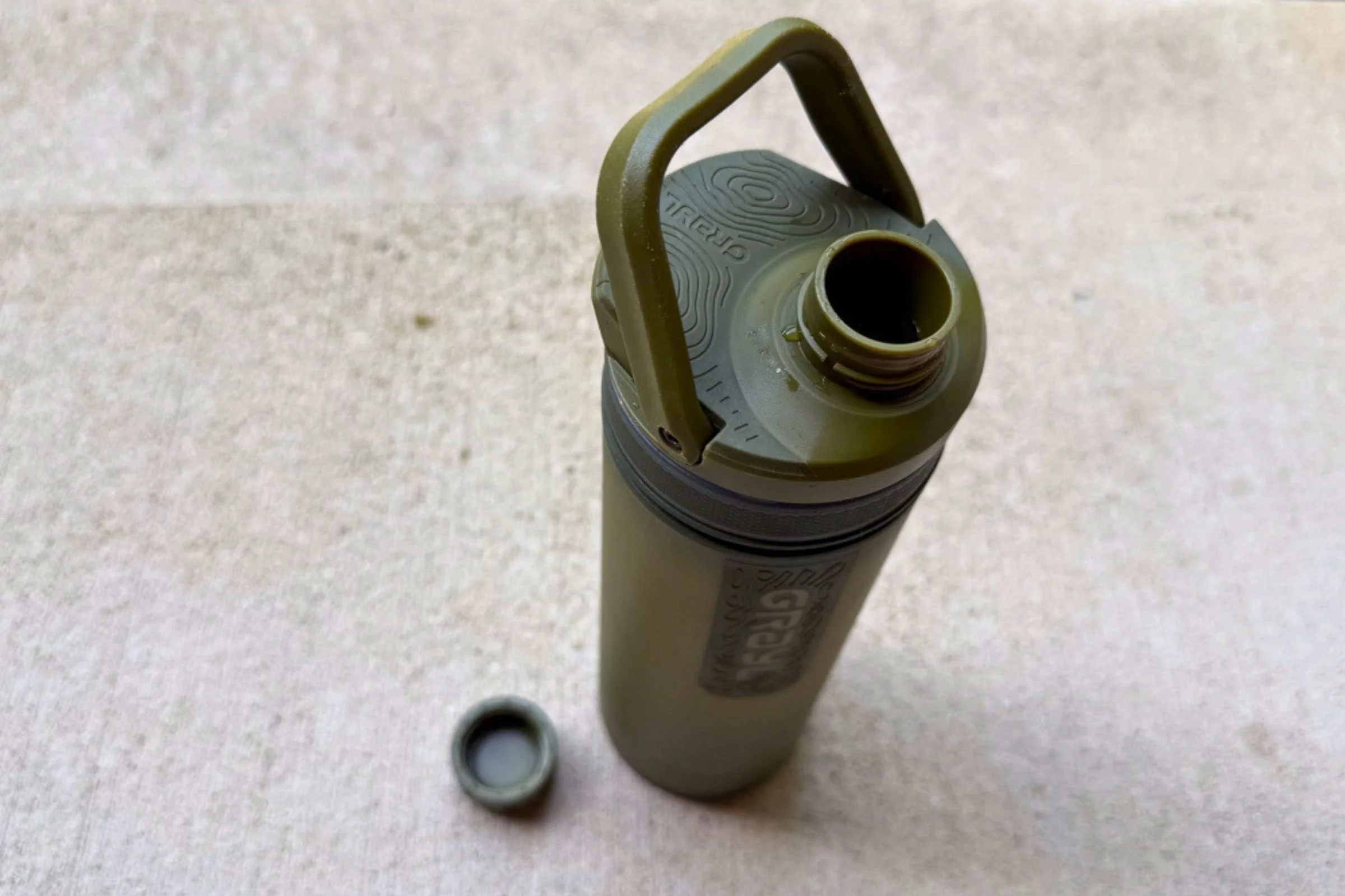 A close-up, high-angle shot of Grayl UltraPress Filter and Purifier Bottle with its cap off to the side.