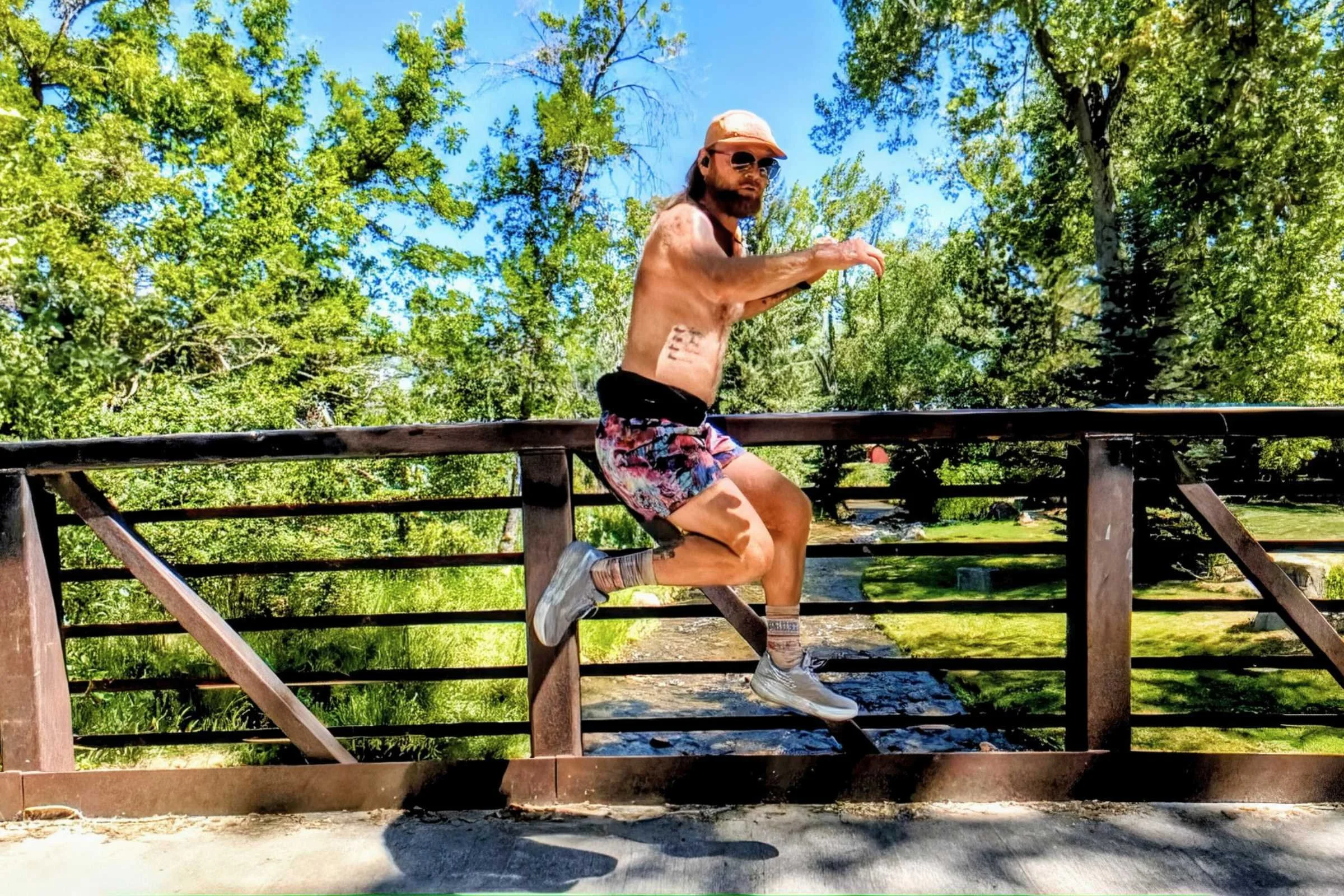 A man wearing Janji AFO Middle Running Shorts jumps on a bridge in a park.