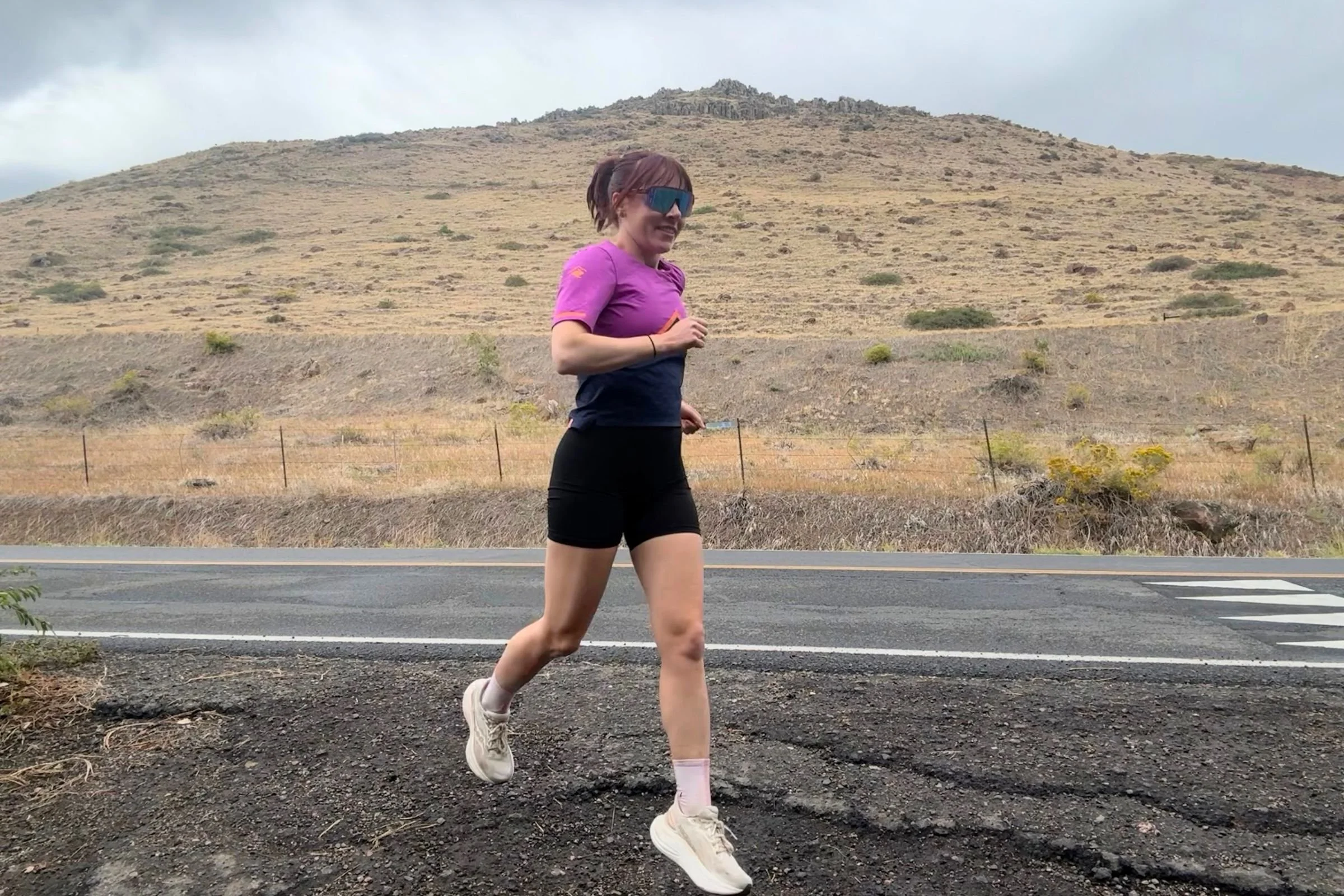 A woman in a pink shirt and shorts running on a road in the Saucony Triumph 24 Road Running Shoe.