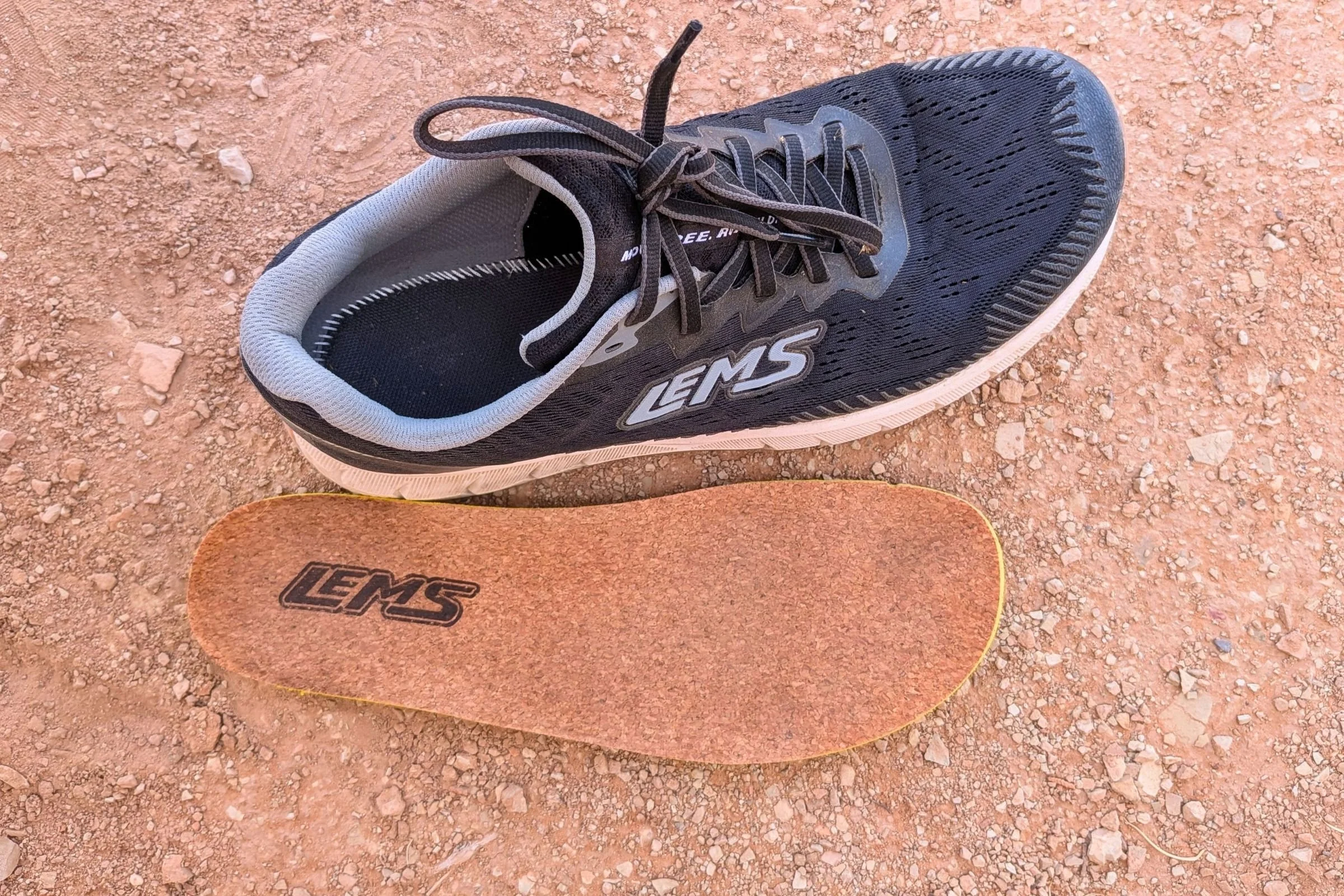 The ZENSPEED+ cork insoles removed from the shoe, sitting next to the shoe, on a hard-packed desert dirt road.