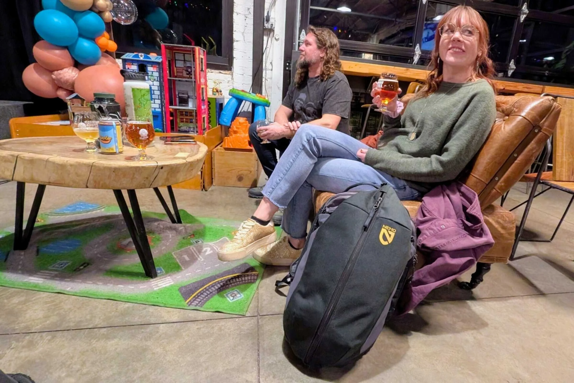 Woman sitting at a brewery with the NEMO Vantage 30 L Pack propped up next to her