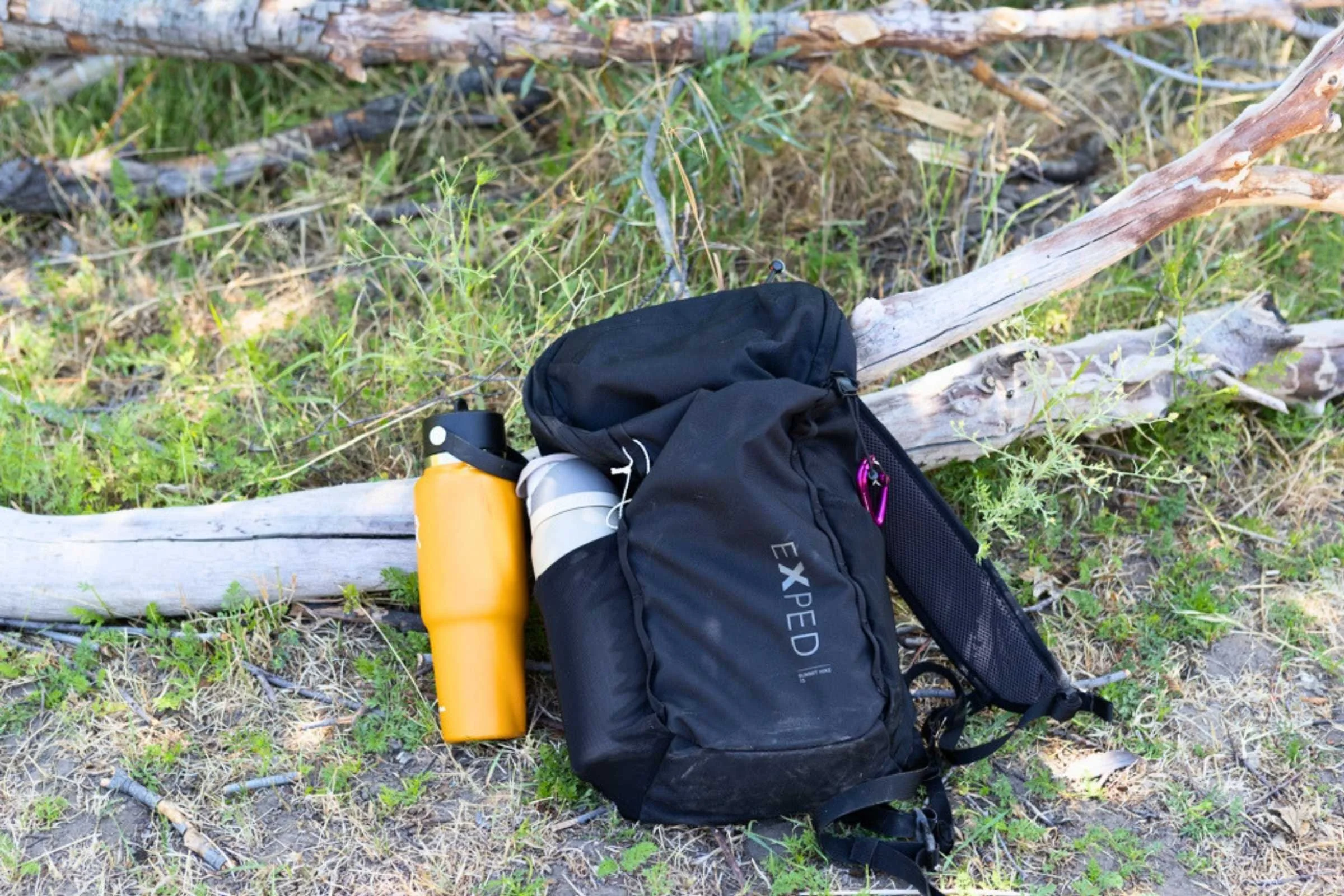 The Exped Summit Hike 15 Pack rests on the trail with a water bottle in its exterior pocket, highlighting its compact size and practical design for shorter hikes.